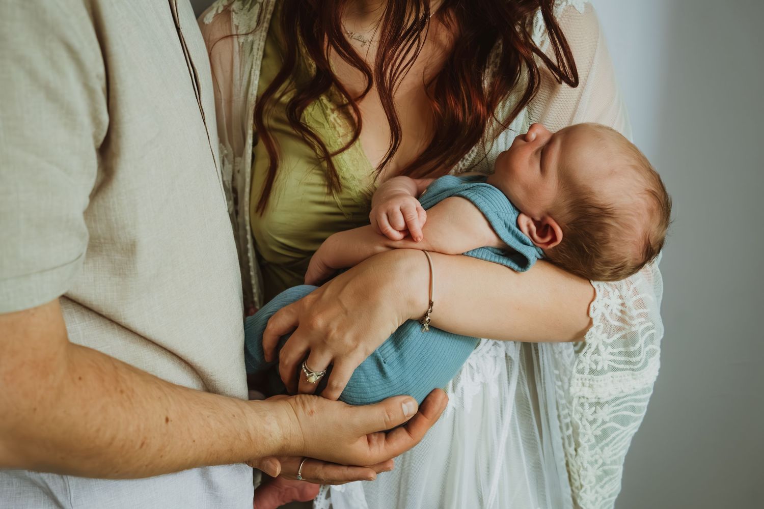 Parents cradling a sleeping newborn baby wrapped in a blue swaddle blanket.
