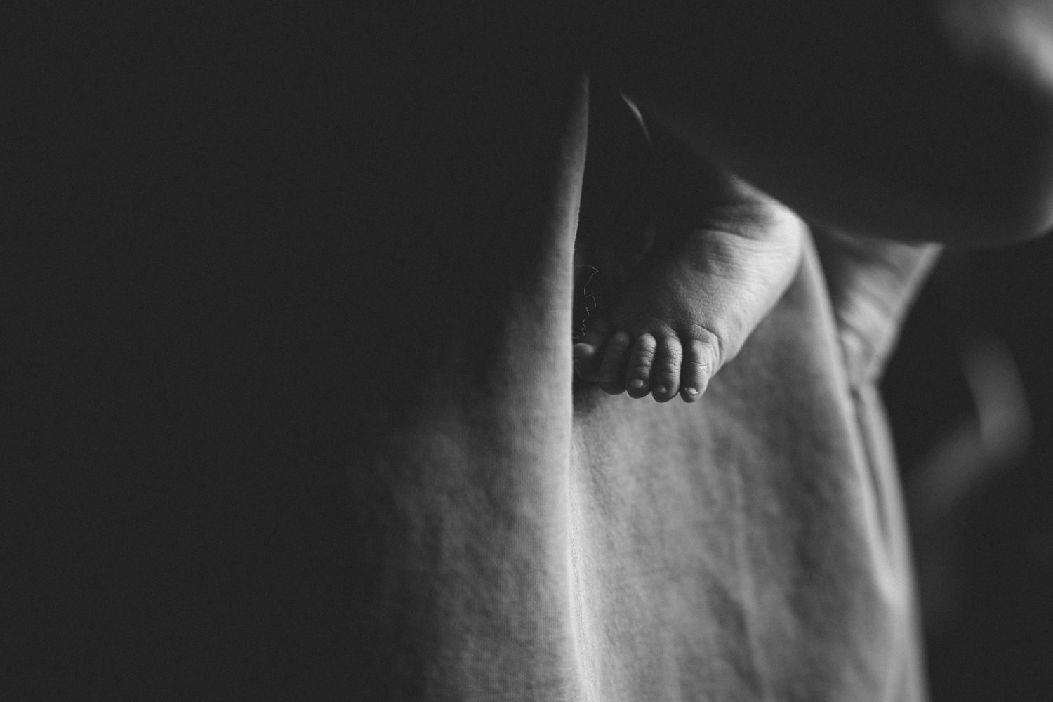 Black and white close-up of tiny newborn baby feet peeking out from soft fabric wrap.
