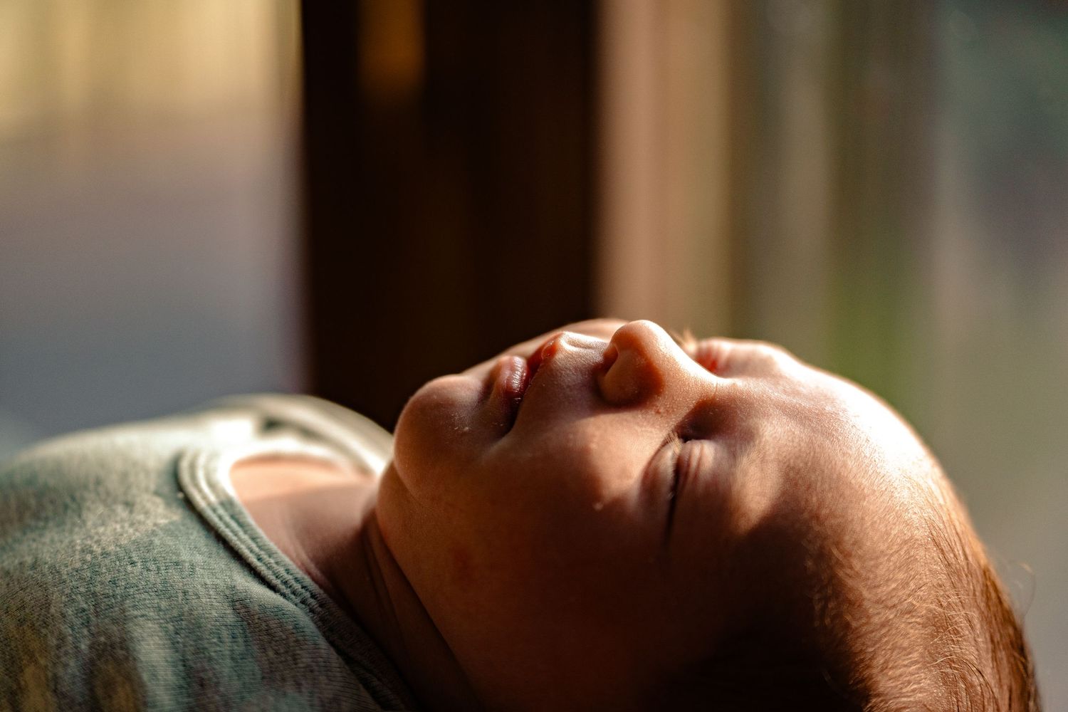 Close-up of a peaceful newborn baby sleeping in warm sunlight, eyes closed and face relaxed.