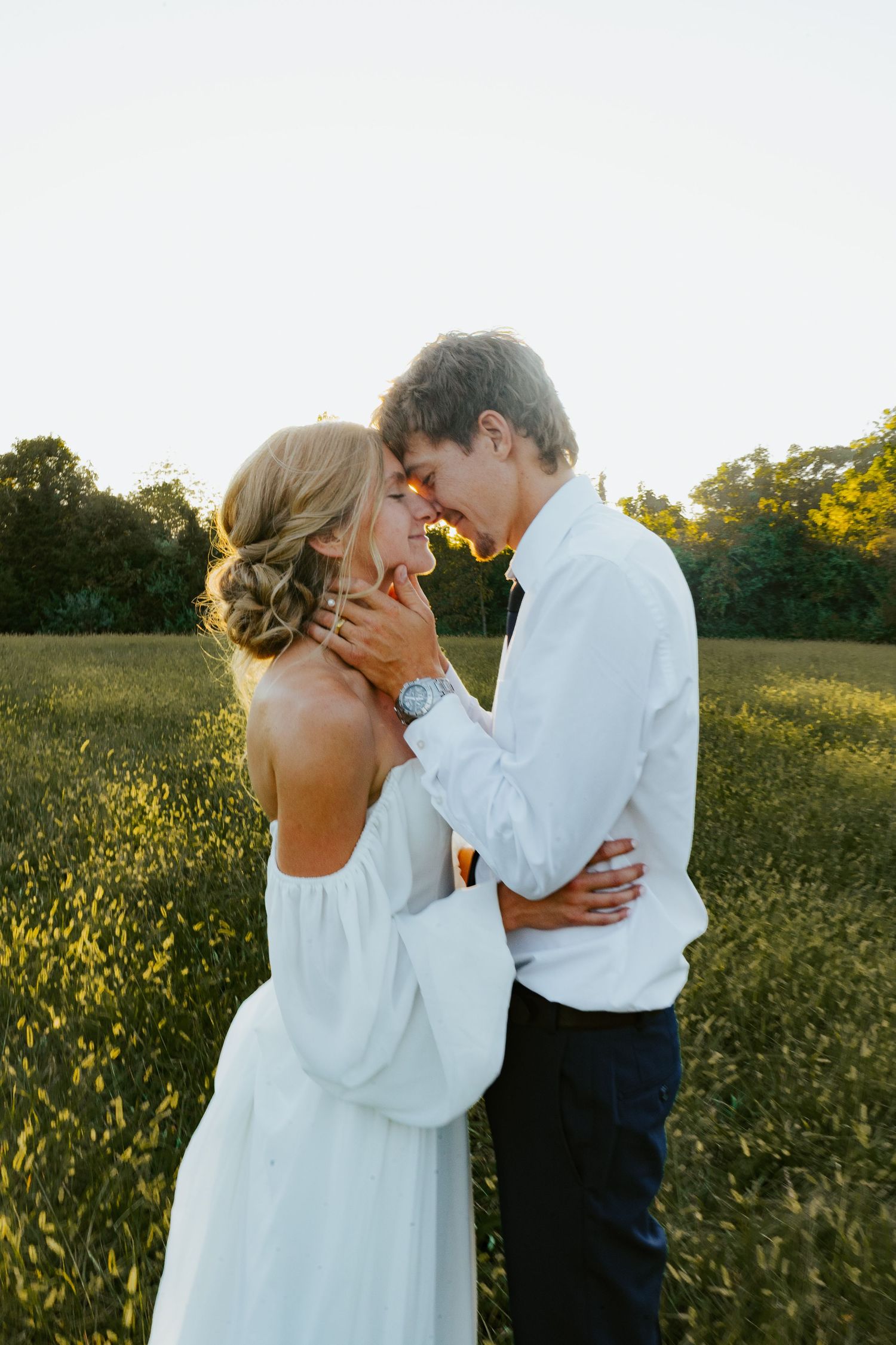 Romantic couple portrait in golden sunlit field with white dress and formal attire.