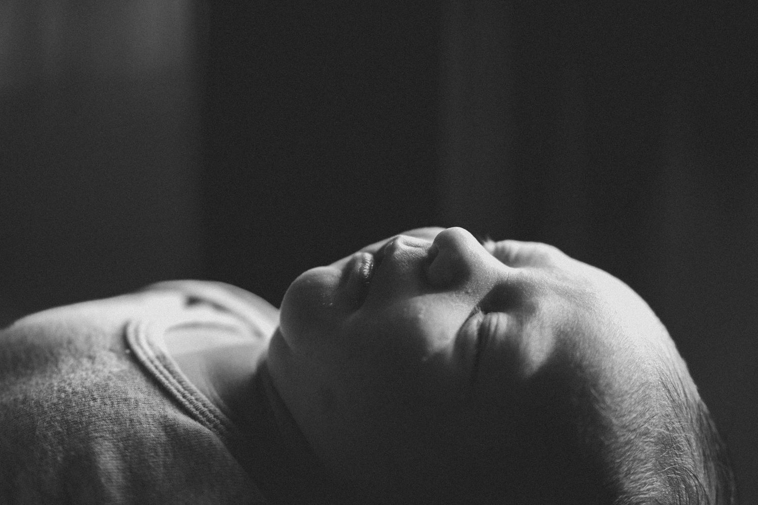 Black and white close-up of a person lying down with eyes closed, peaceful expression in soft dramatic lighting.