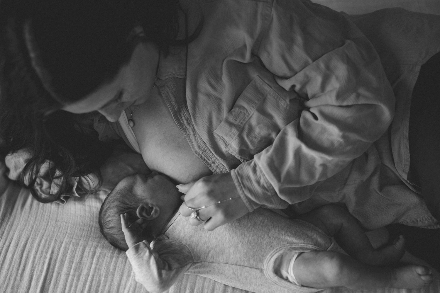 Black and white image of mother lying down lovingly gazing at her newborn baby on a bed.