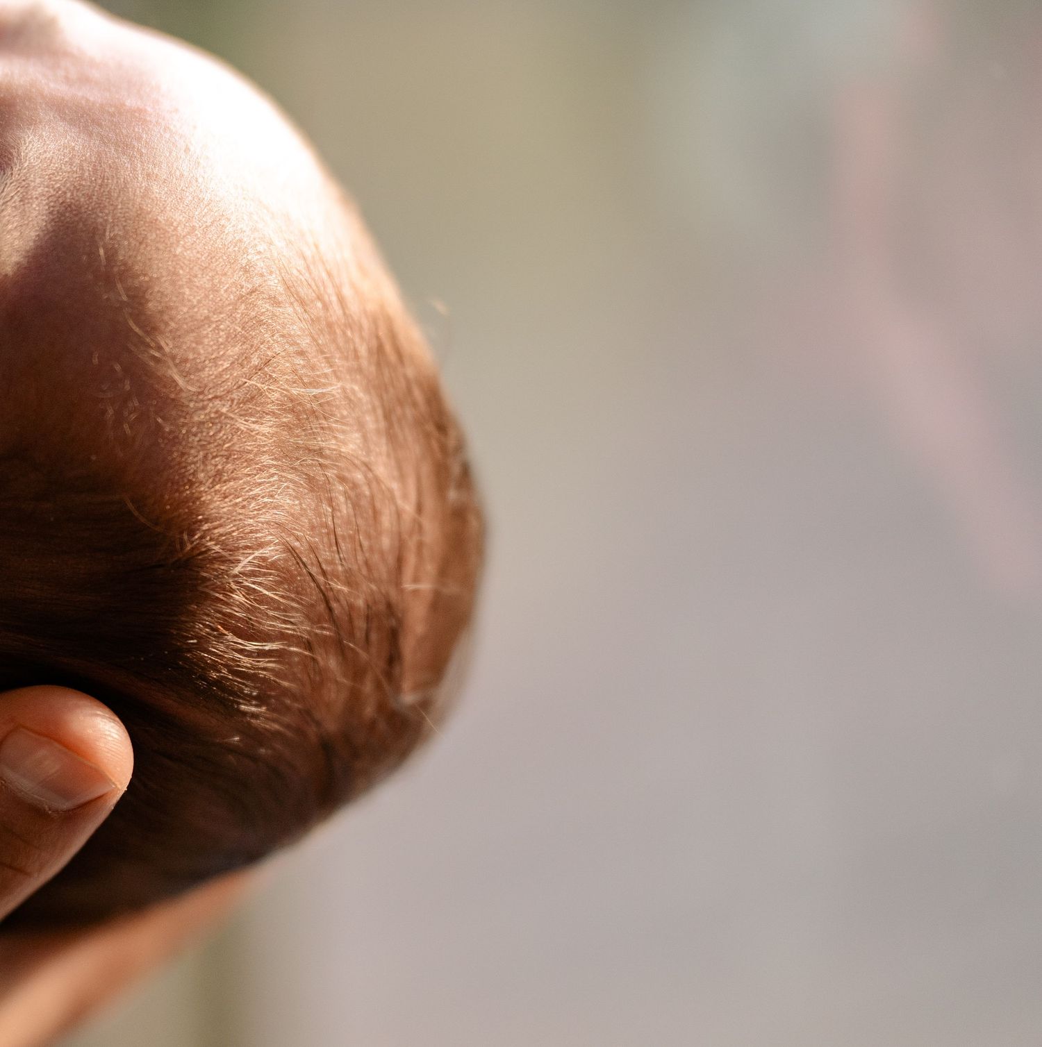 Close-up of newborn baby head with fine hair being gently supported by parent hand.
