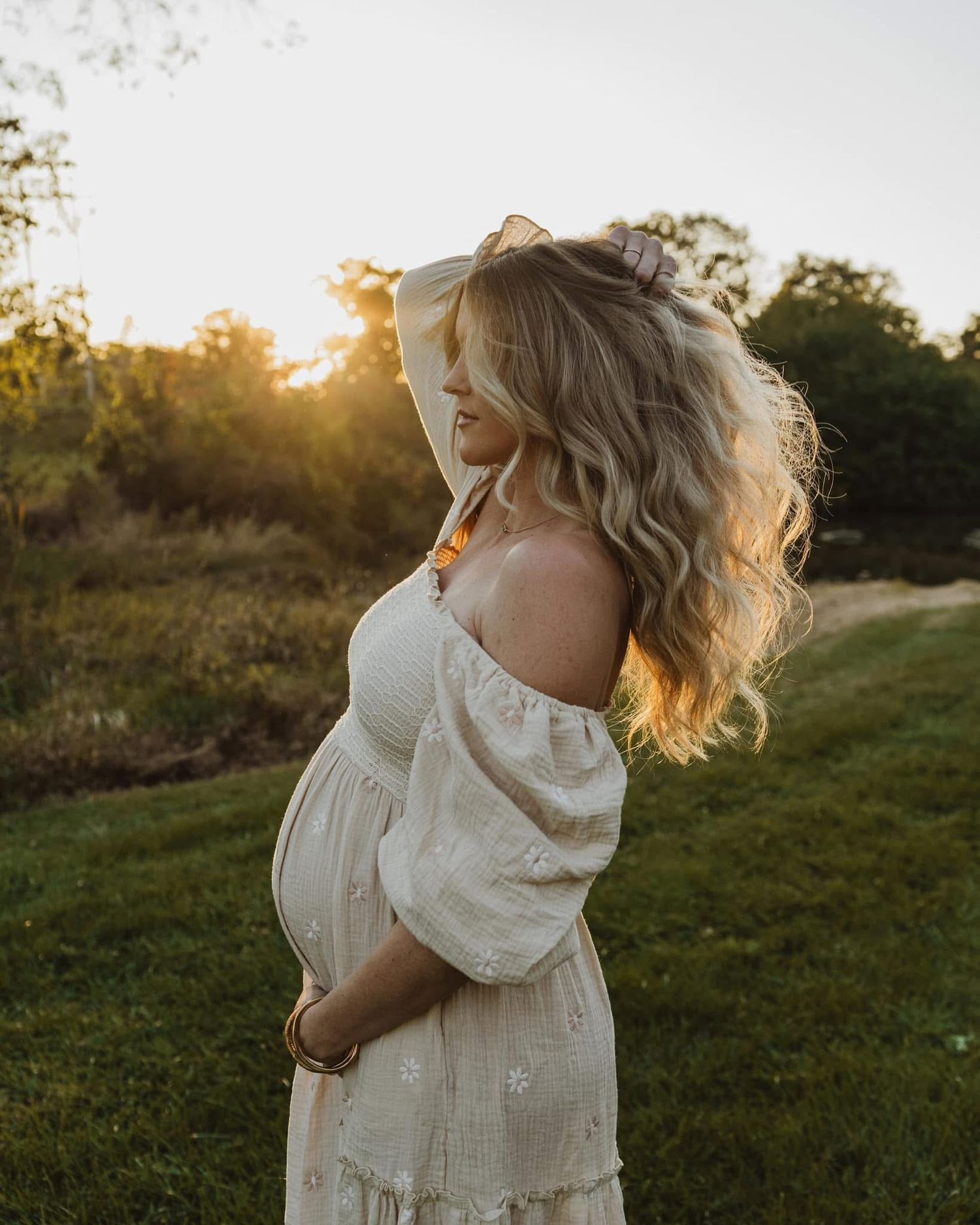 Woman in white dress twirling in sunlit field during golden hour.