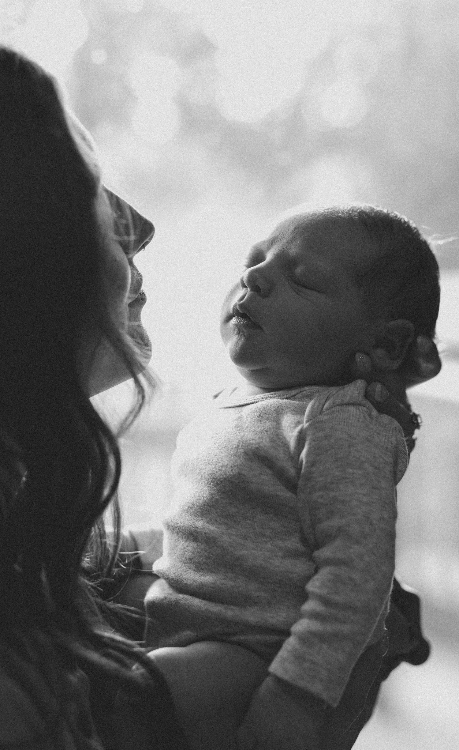 Black and white photo of a mother gazing lovingly at her sleeping newborn baby.