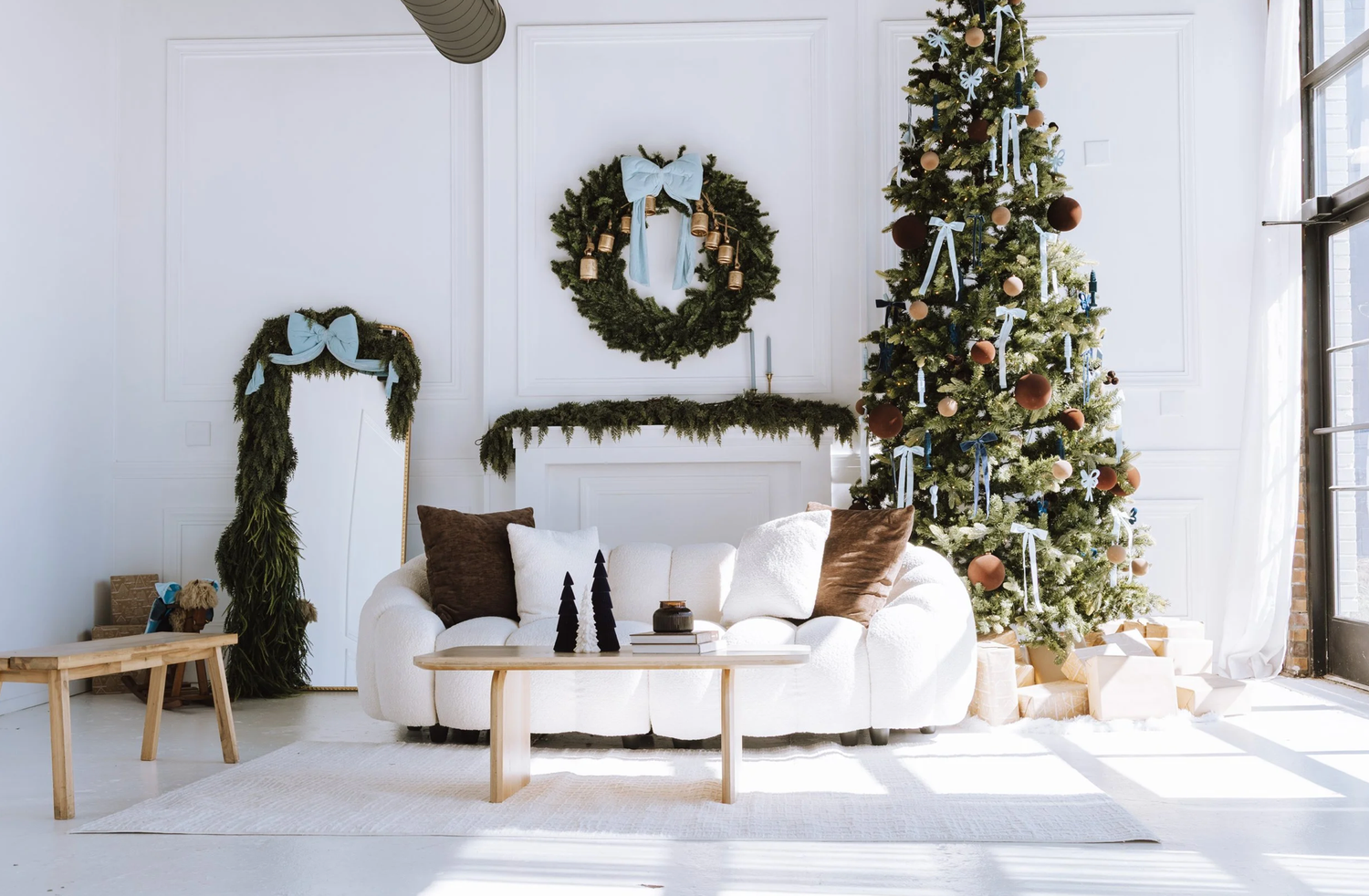 Festive living room with white sofa, decorated Christmas tree, garland, and wreath in a bright white interior.