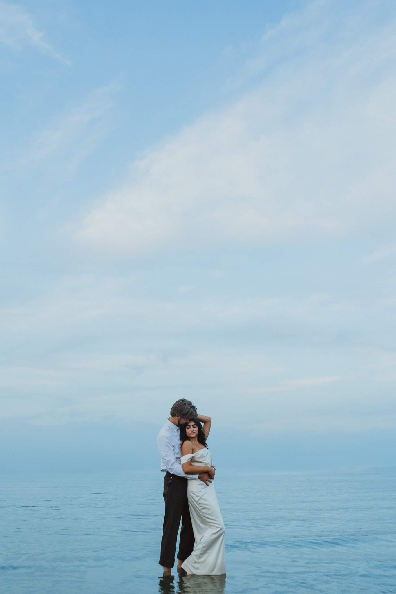 Romantic couple embracing against serene ocean horizon and blue sky backdrop.