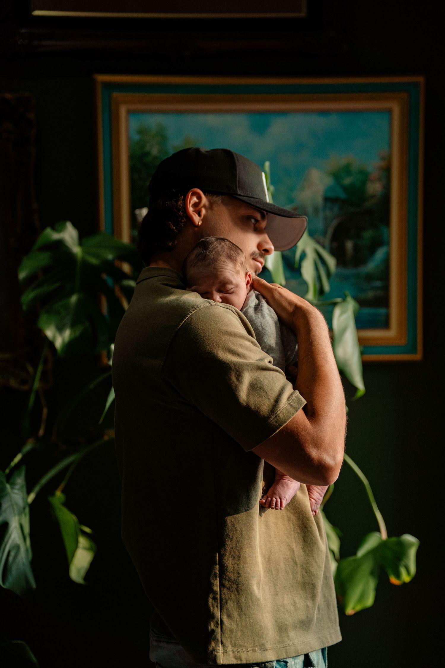 A tattooed father tenderly holds his newborn baby against his chest indoors.