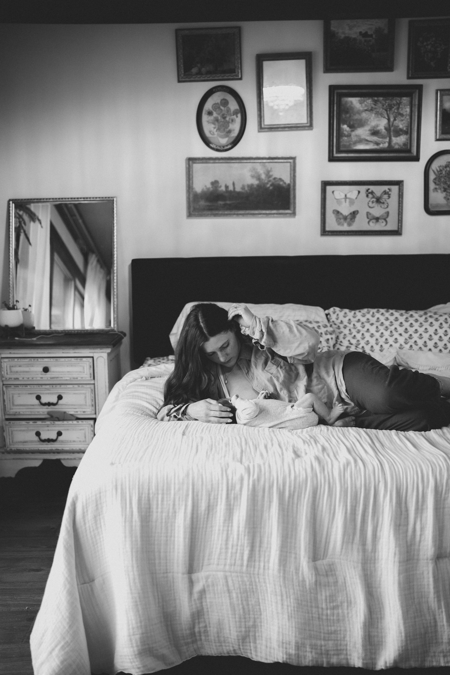 Black and white photo of new mother lying on bed gazing lovingly at her newborn baby.