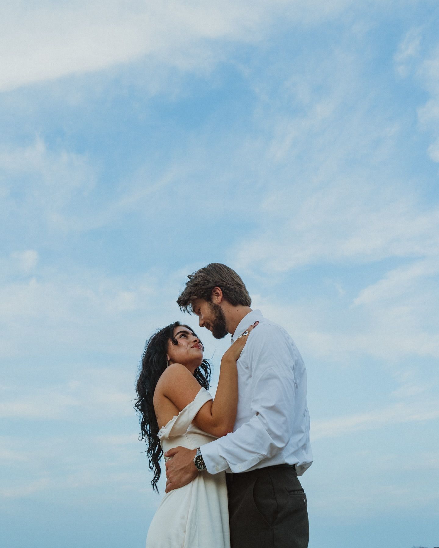Couple sharing intimate moment against bright blue sky background.