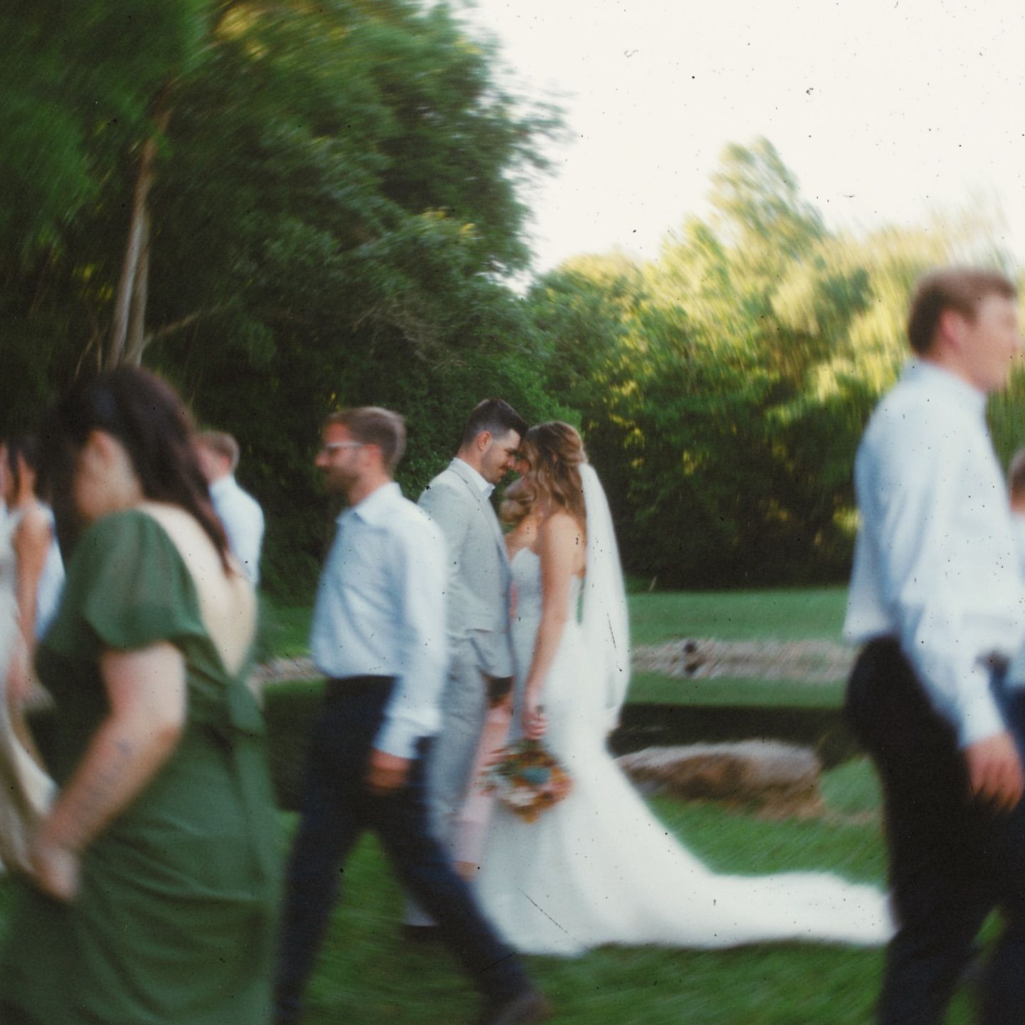 Motion-blurred group of people in formal attire walking outdoors at dusk.