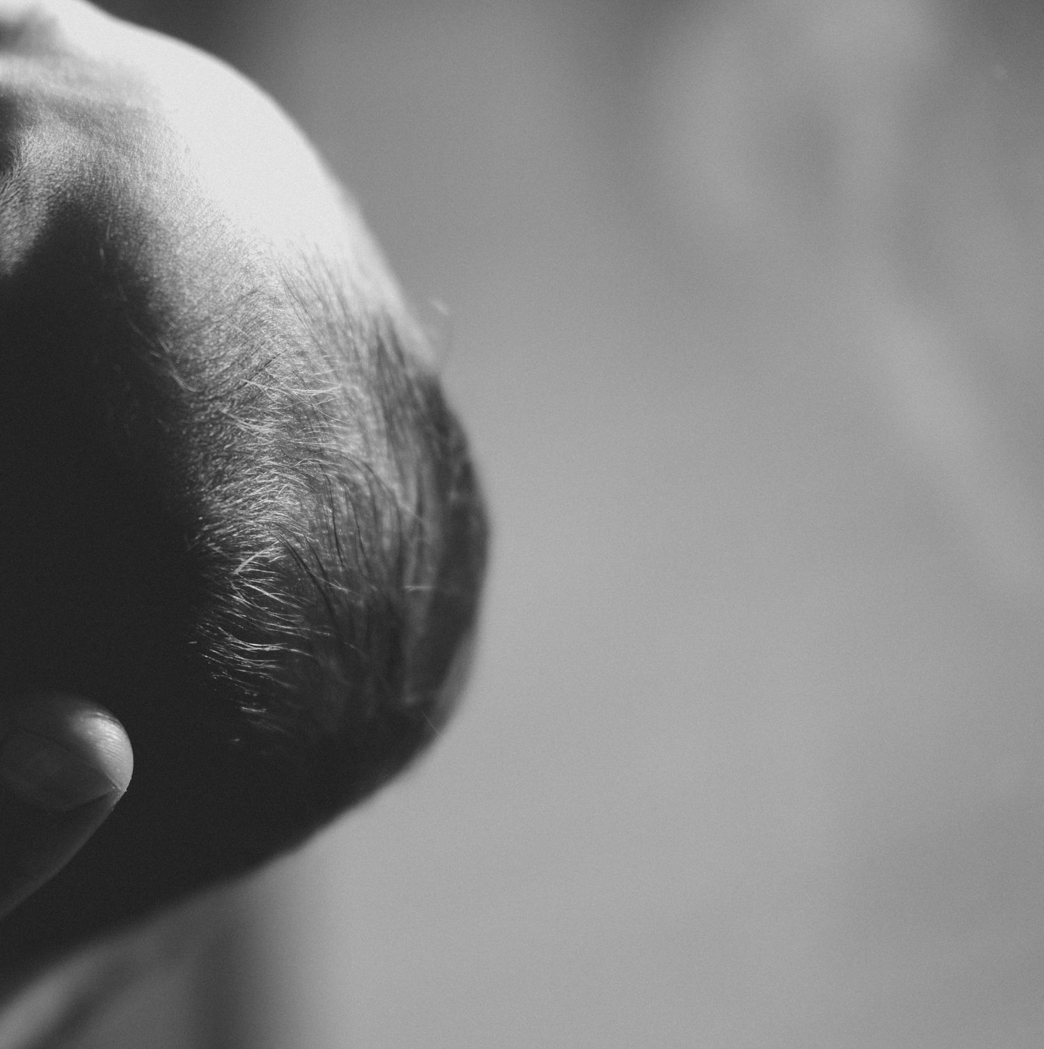 Close-up black and white photo of a newborn baby's head with fine dark hair.