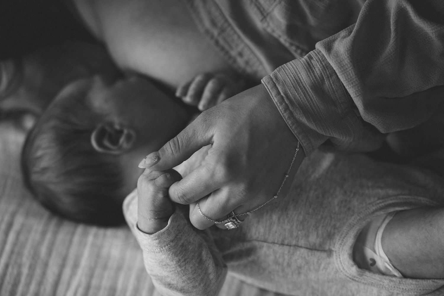 Black and white image of parent gently holding newborn babys tiny hand on soft surface.