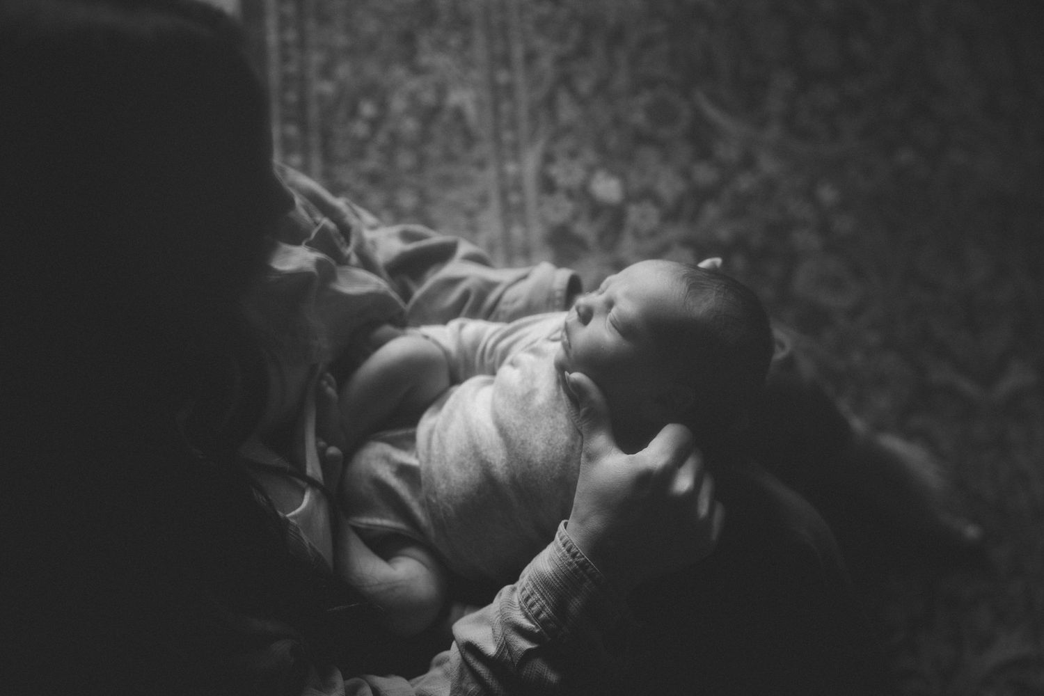 Black and white photo of a newborn baby being cradled in loving arms, swaddled in a soft blanket.