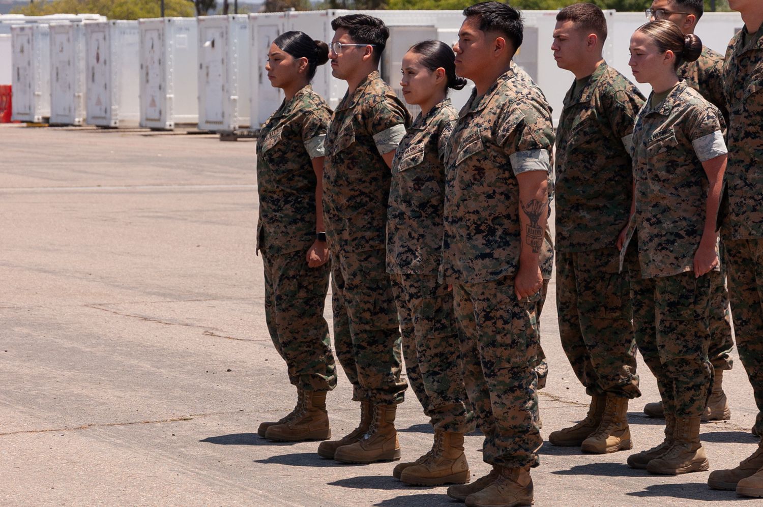 US Marines in camouflage uniforms standing at attention in formation on sunny airfield.