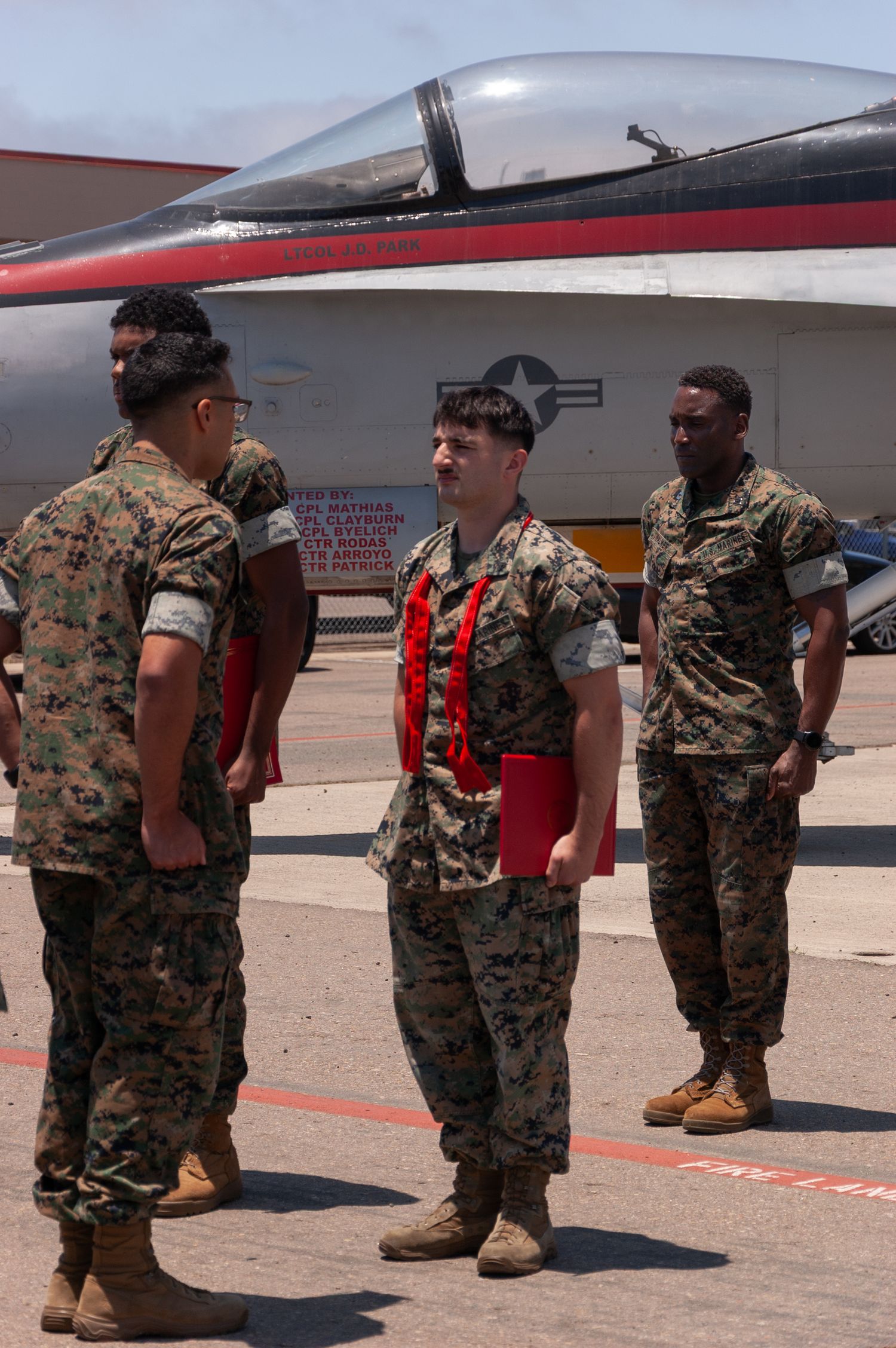 US Marines in camouflage uniforms conversing near military jet aircraft on sunny airfield.