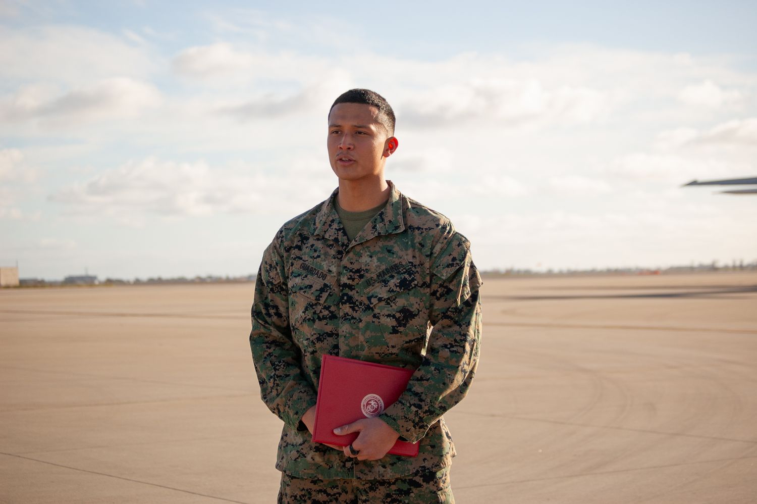 US Marine in camouflage uniform holding red folder speaking to fellow Marines.