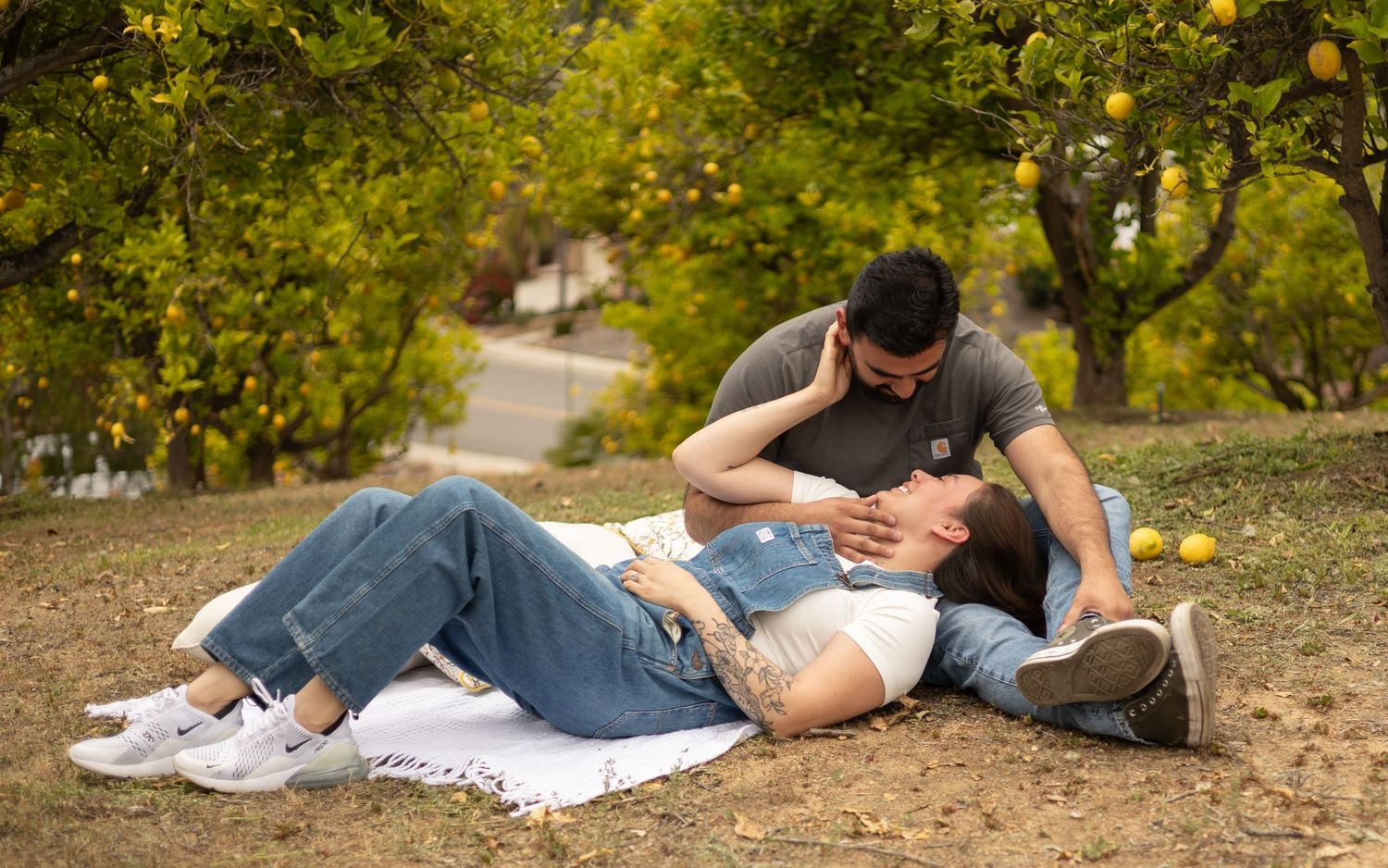 A couple relaxes on a blanket in a citrus orchard, woman lying across mans lap.