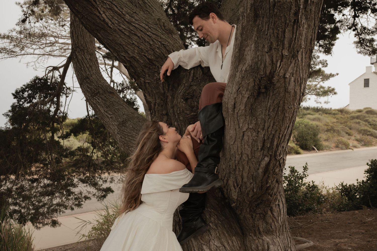 Bride and groom share a romantic moment leaning against a large tree trunk outdoors.