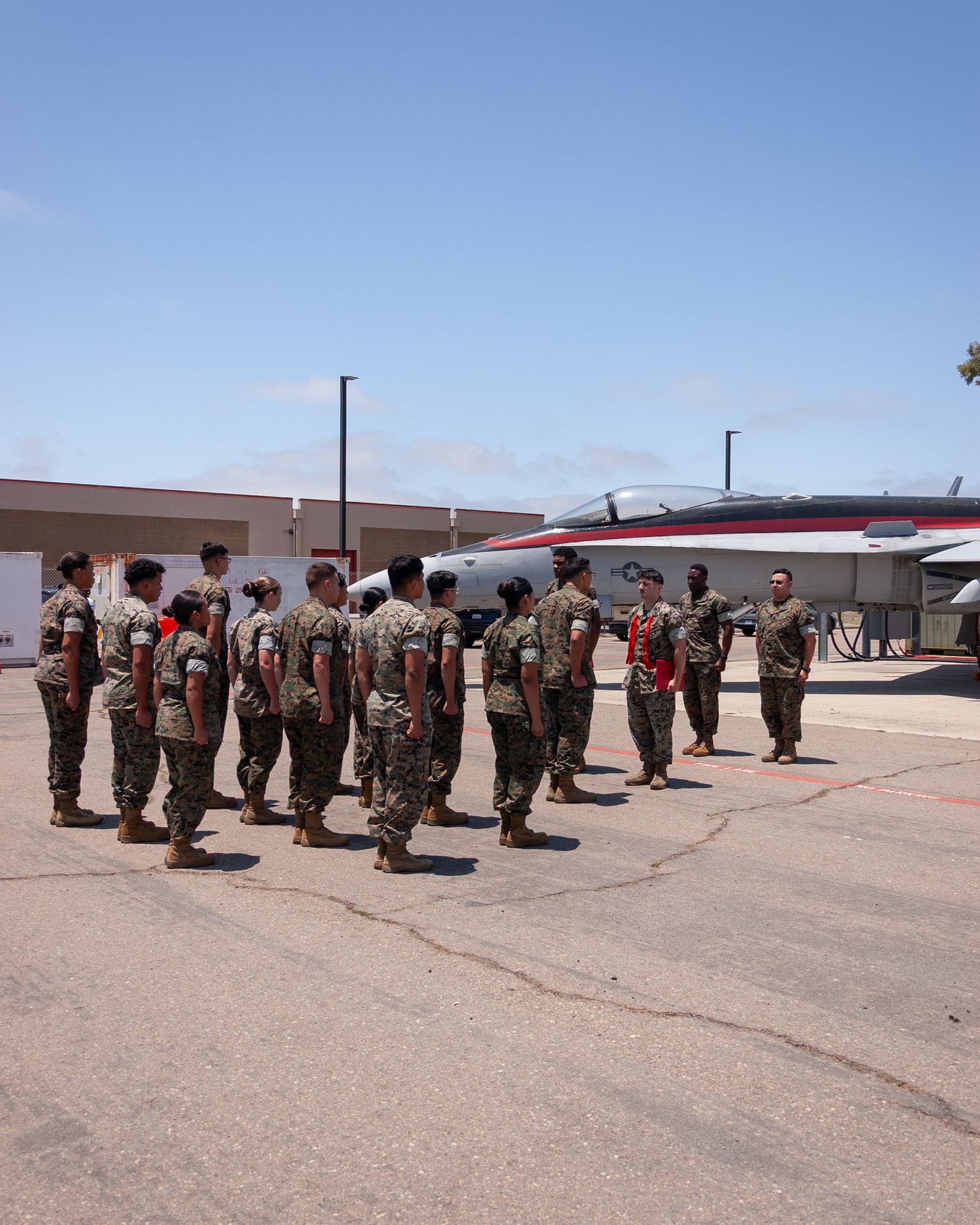 Group of US Marines in camouflage uniforms stand in formation on sunny military airfield.