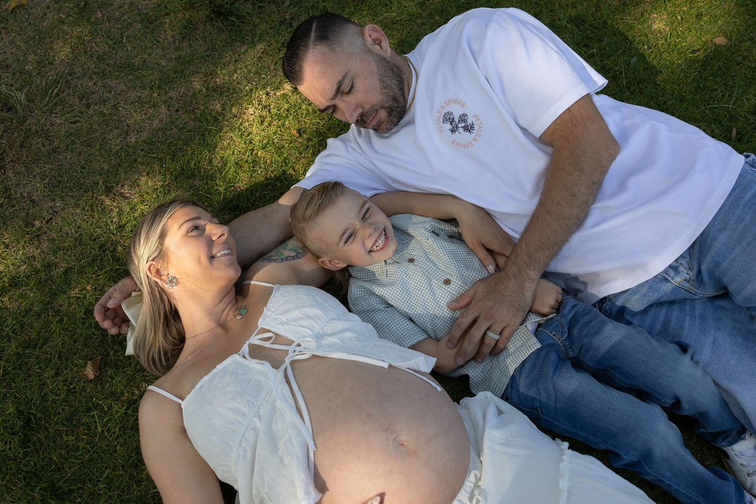 Pregnant woman lying on grass with husband and young child during outdoor maternity photo session.