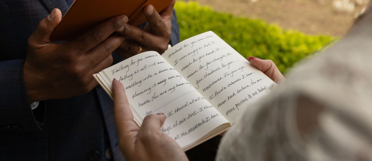 Two people holding an open handwritten journal or notebook outdoors in natural light.