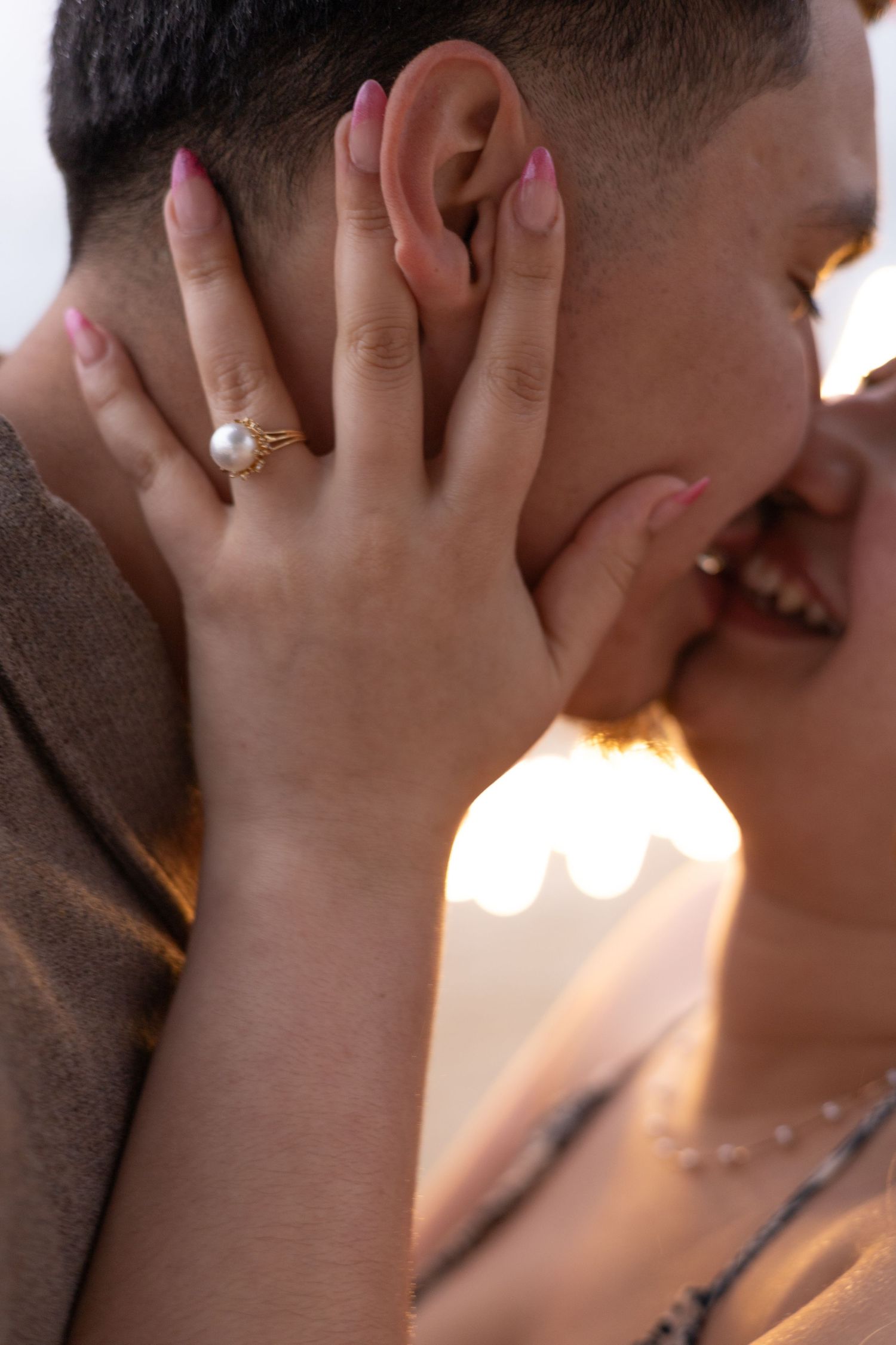 Close-up of couple sharing a kiss with a pearl engagement ring visible on her hand.