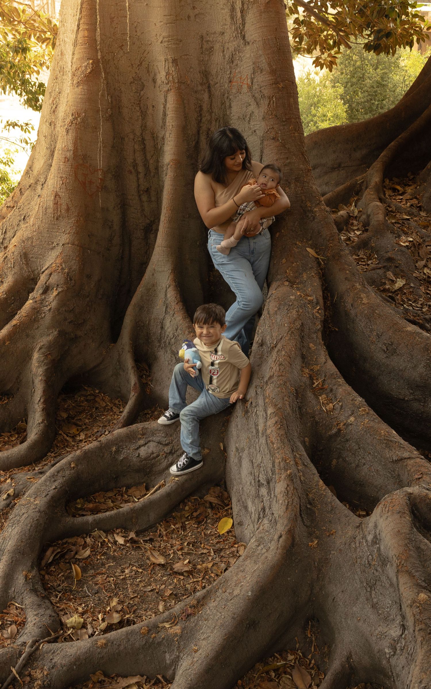 Mother and two children posing among massive tree roots in a forest park setting.