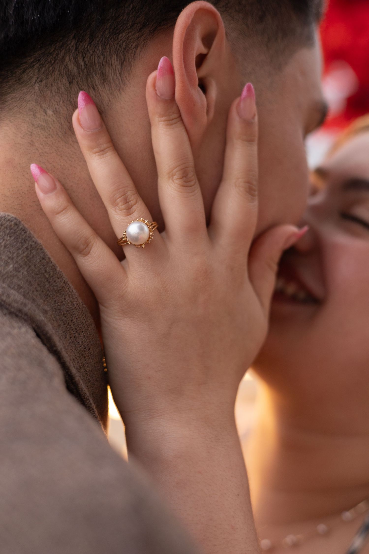 Close-up of a pearl ring in gold setting on a womans hand with pink nails.