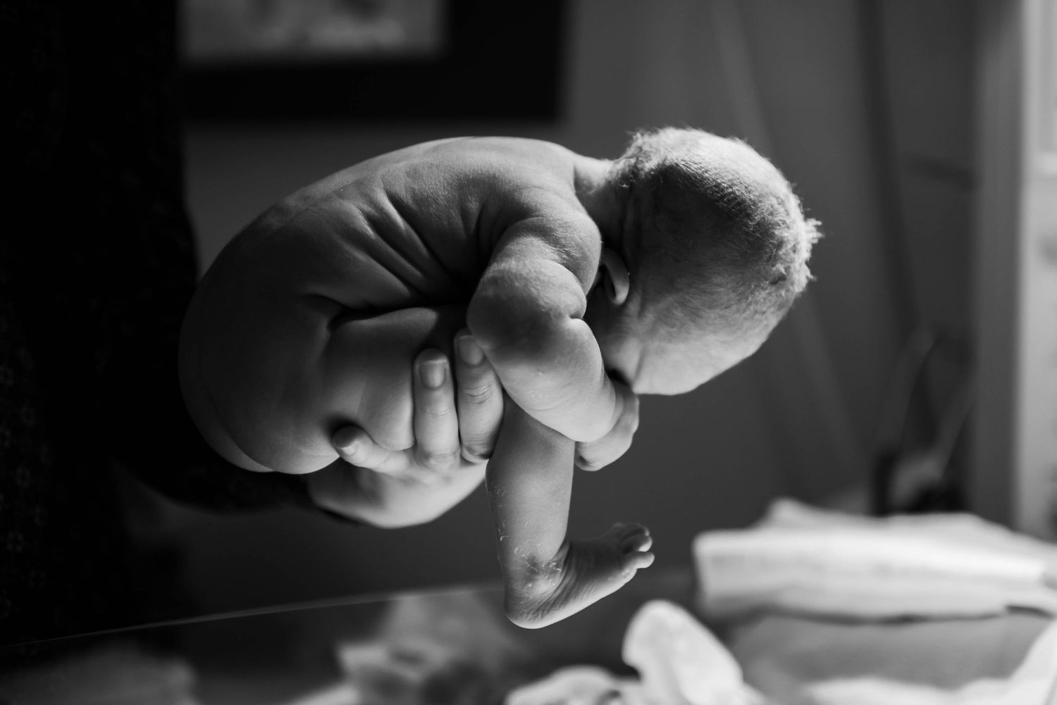 Black and white close-up of a newborn baby being held in one hand, showing tiny curled body.