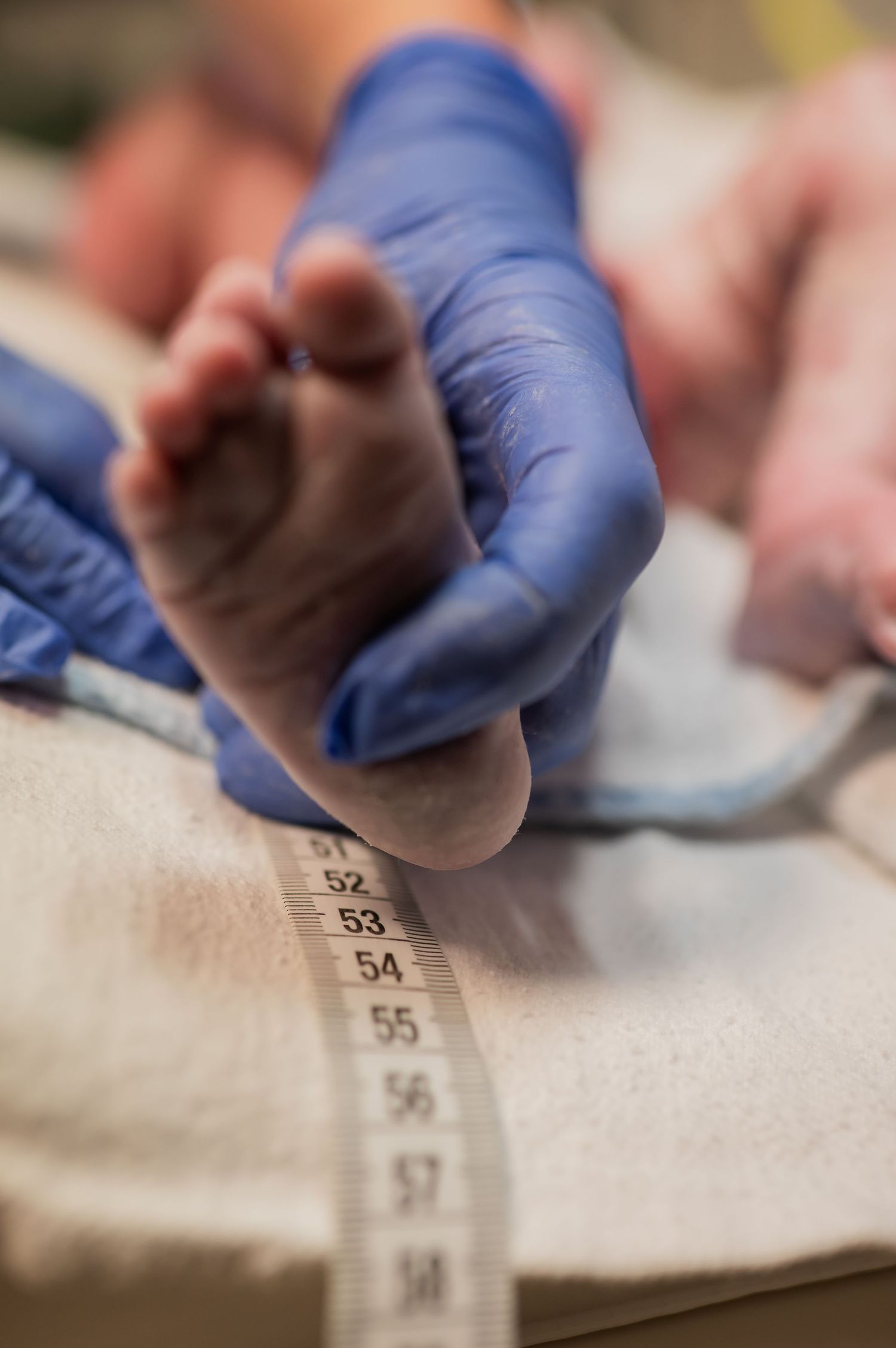 Medical professional measures a newborn baby's foot with a tape measure wearing blue gloves.