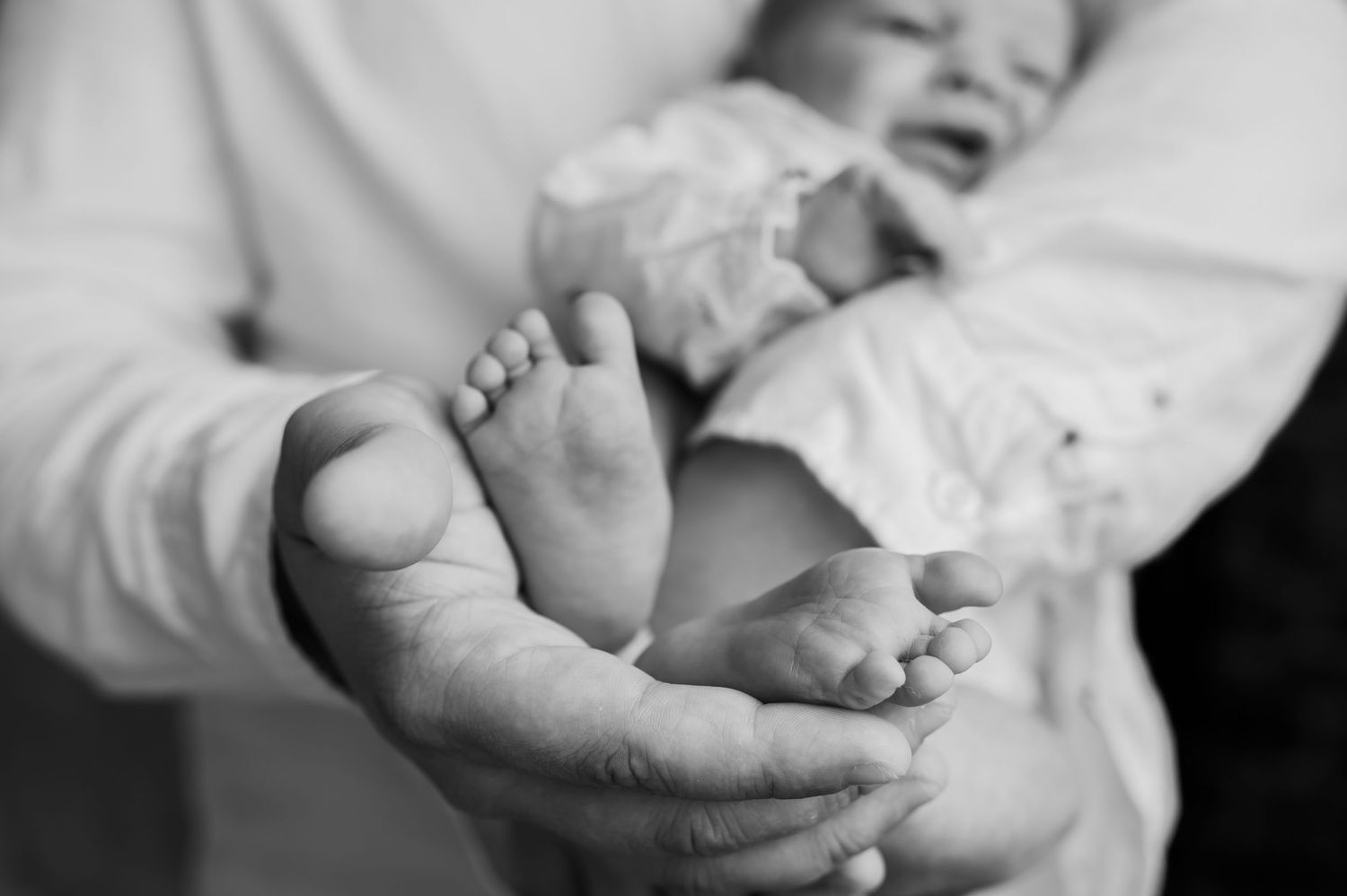 Black and white close-up of newborn baby feet cradled in adult hands.