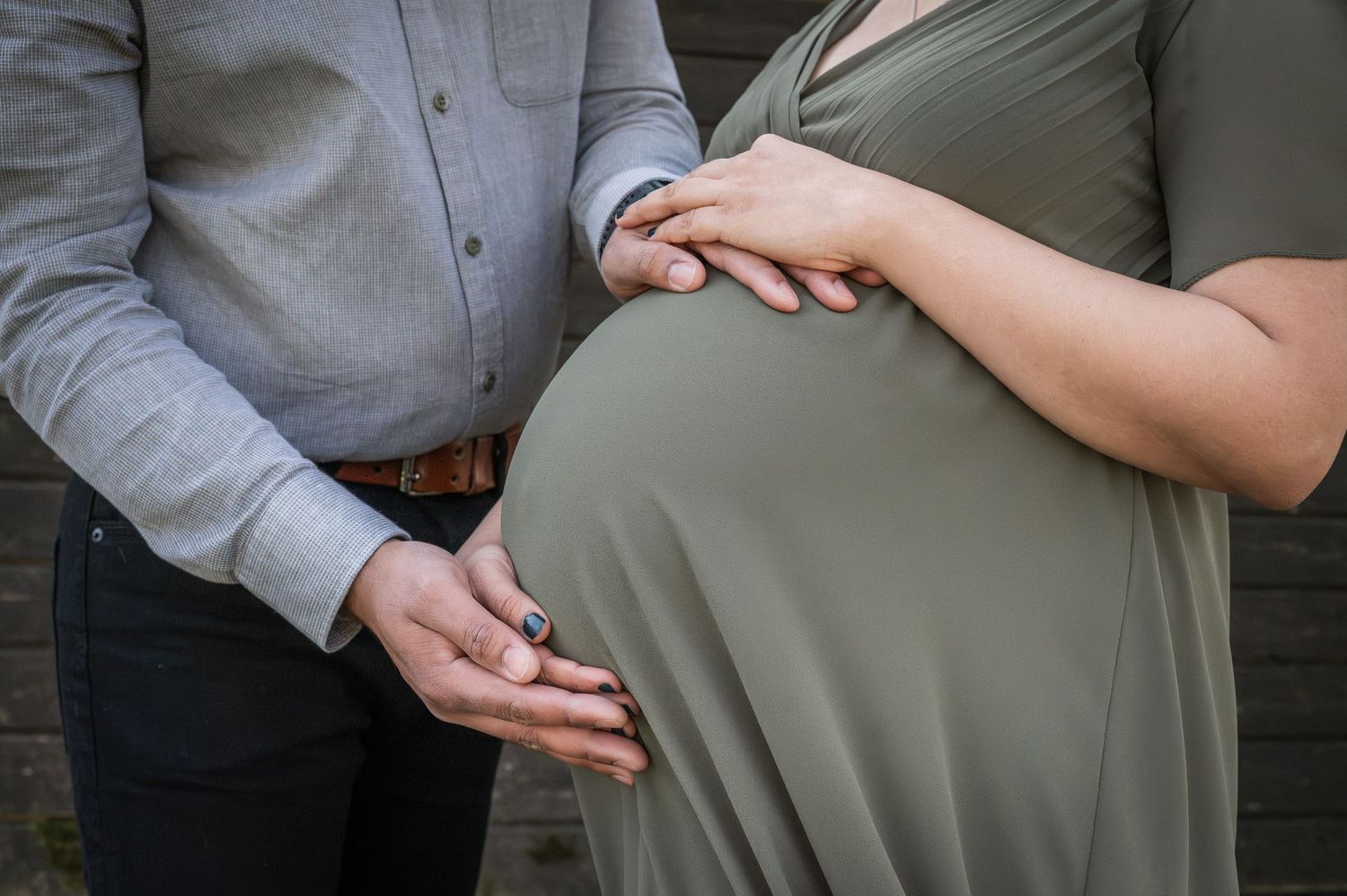 Close-up of couple holding hands over pregnant belly in olive green dress.