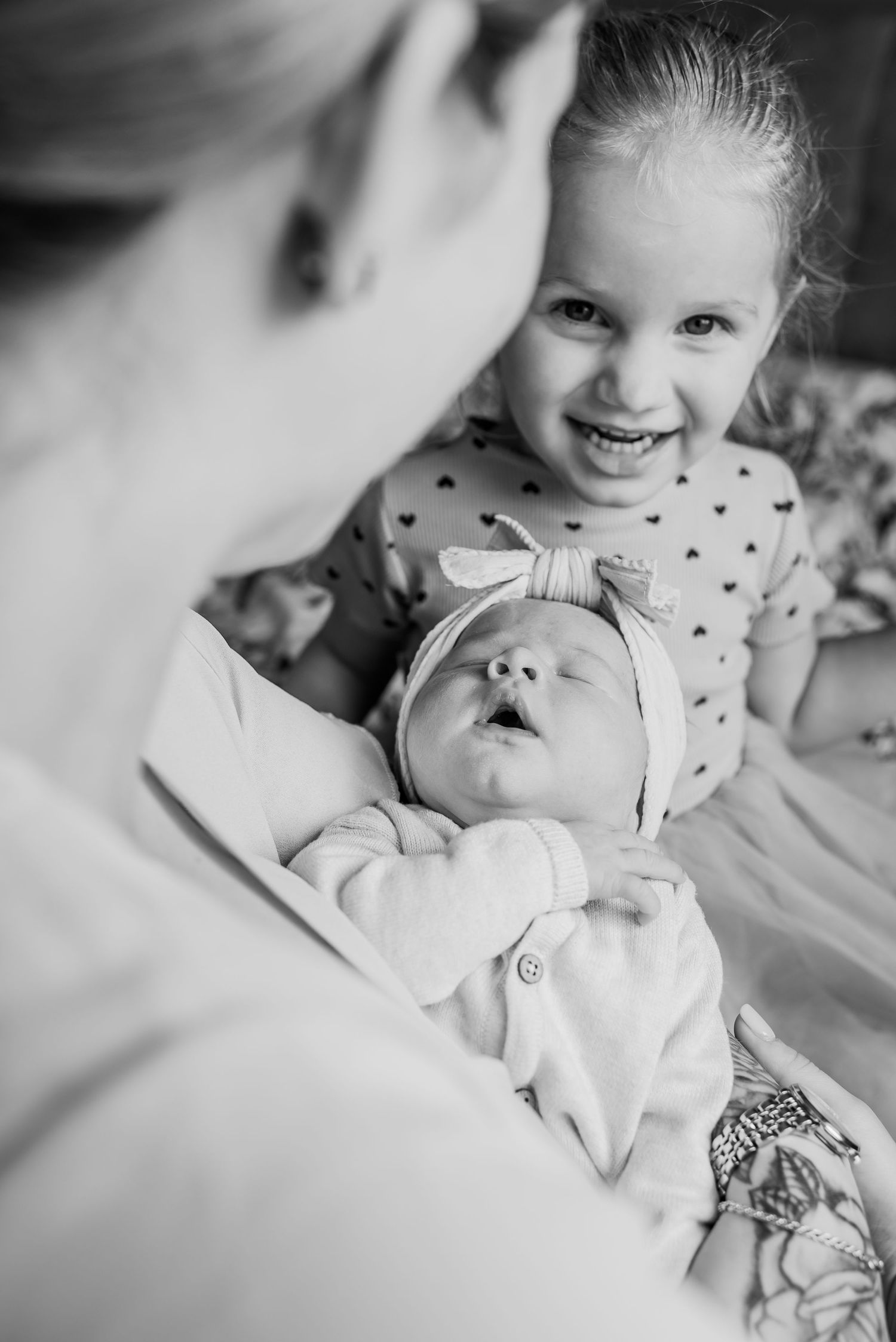 Black and white photo of smiling girl looking at newborn baby held by mother.