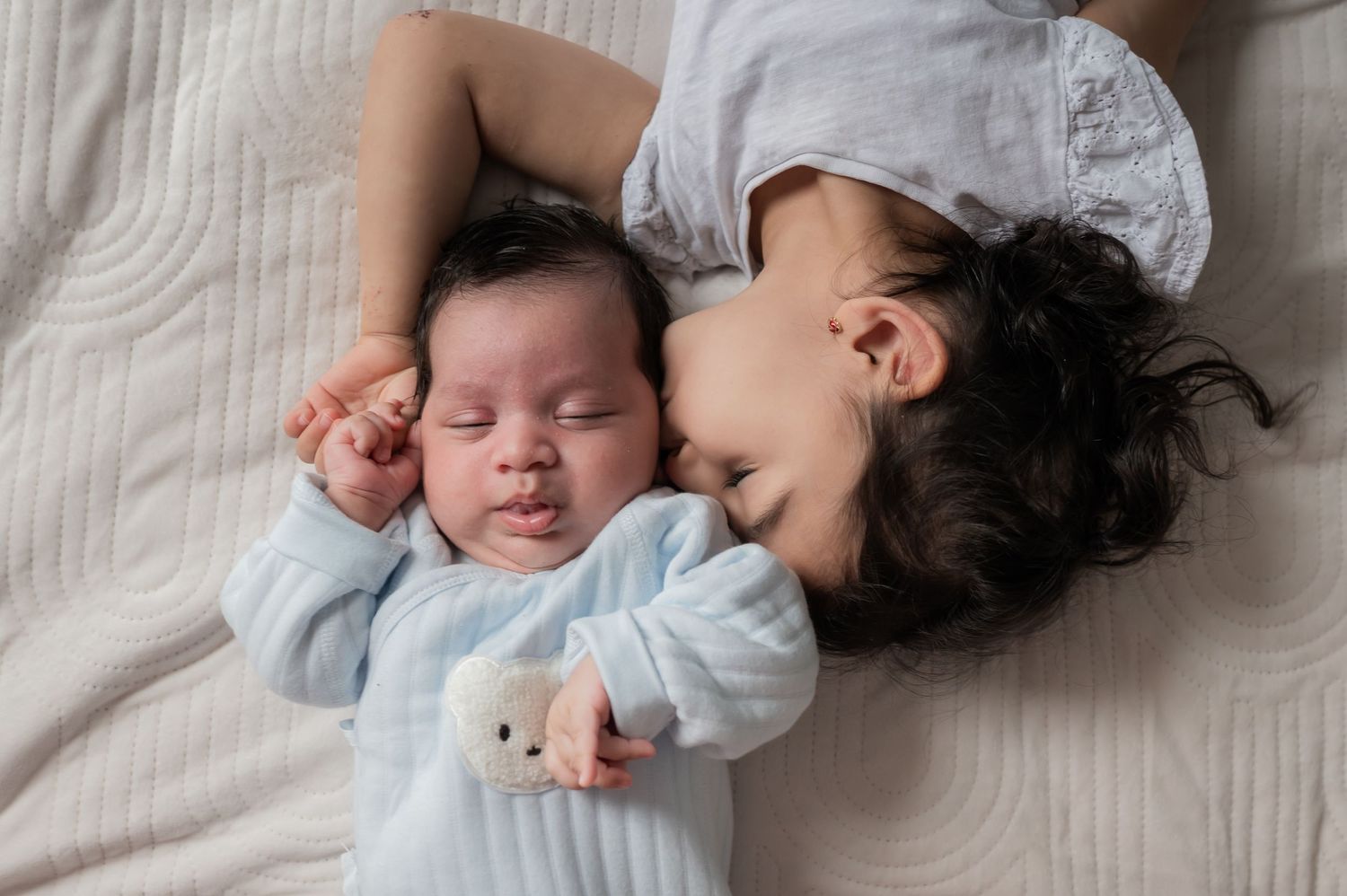 A young child snuggles next to a peacefully sleeping newborn on a soft white blanket. Lelystad, Almere, Dronten, Flevoland