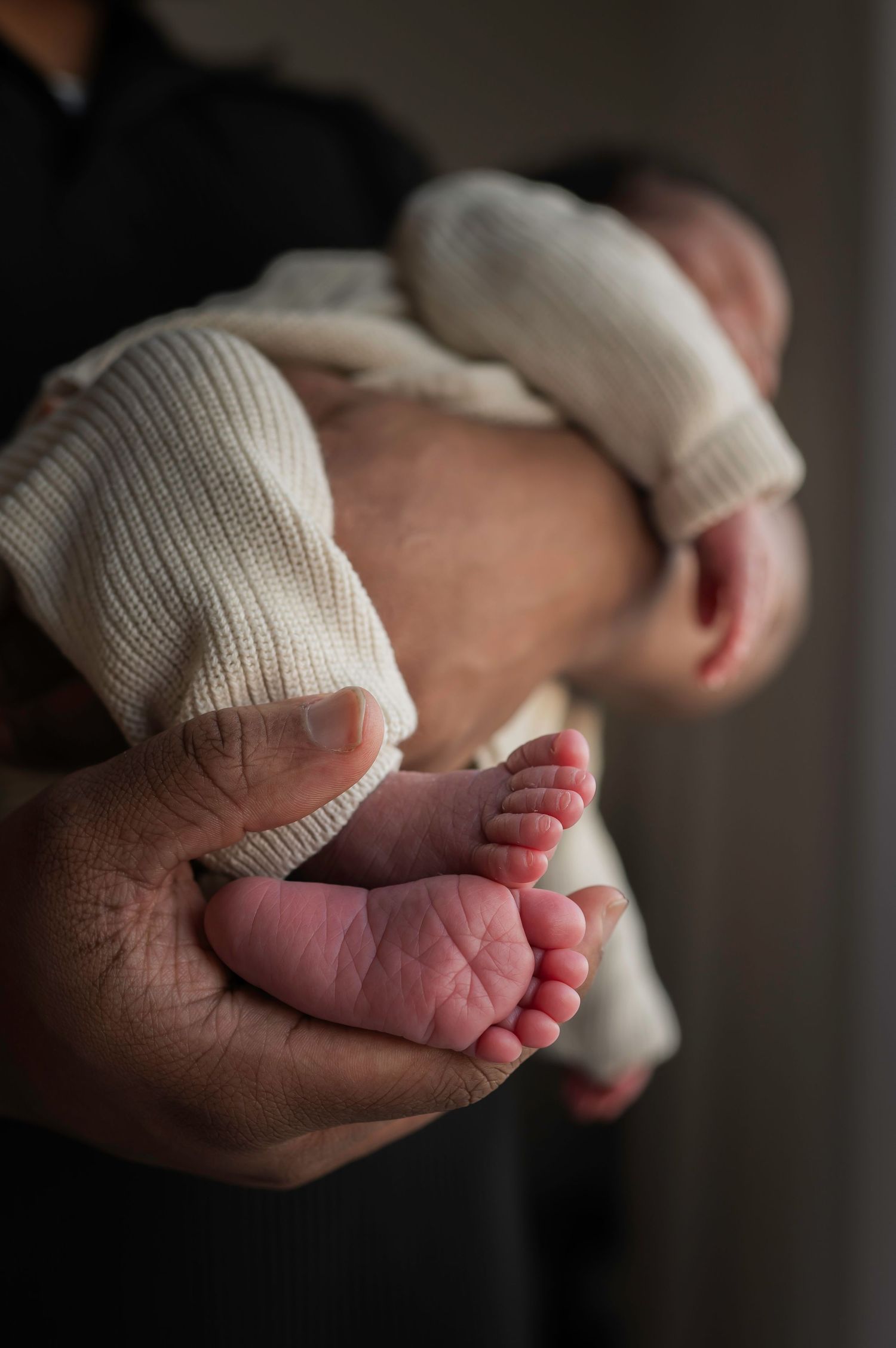 Close-up of a parent gently holding a newborn baby, focusing on the tiny feet and hands.