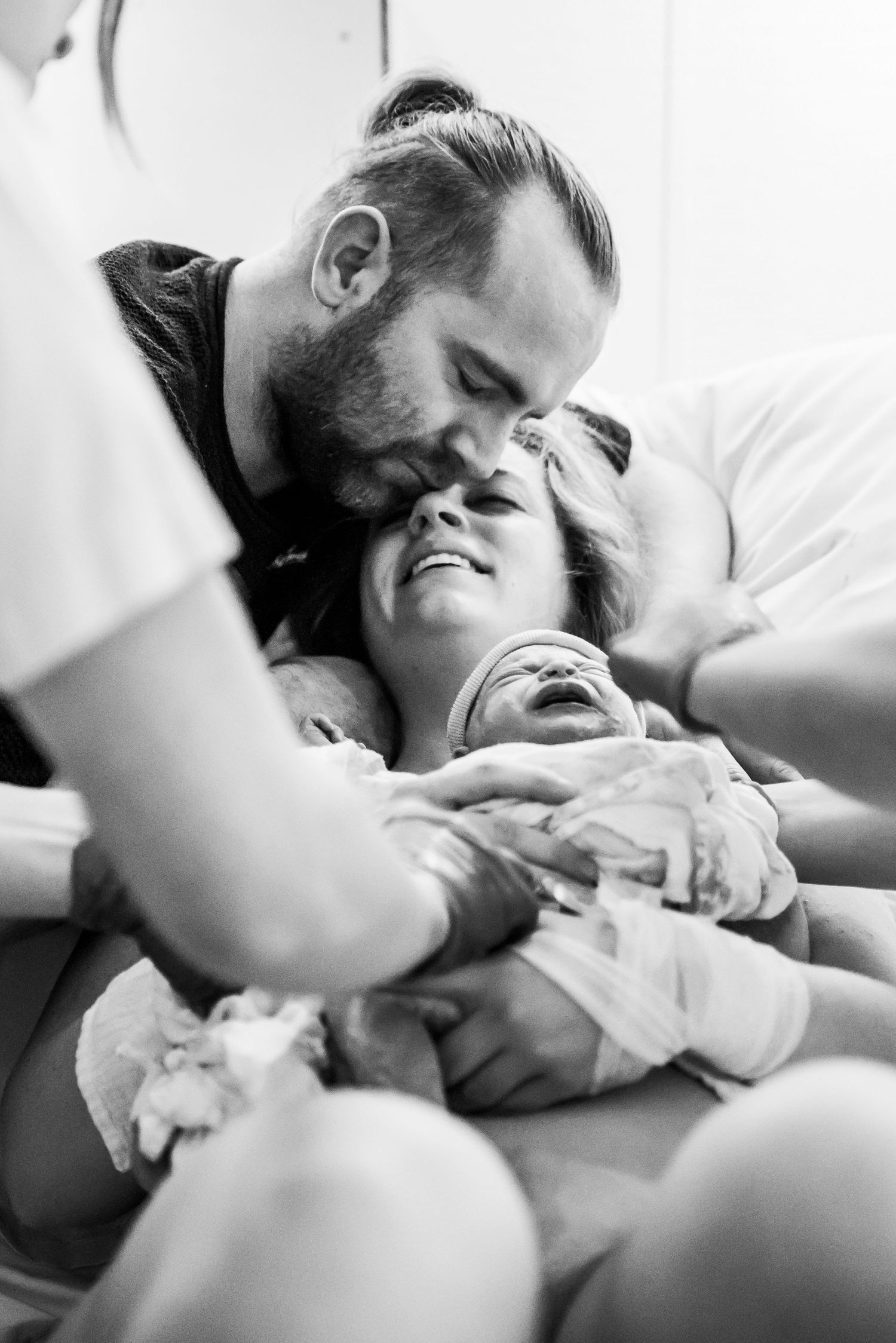 Emotional black and white photo of parents holding their newborn baby after birth in hospital.