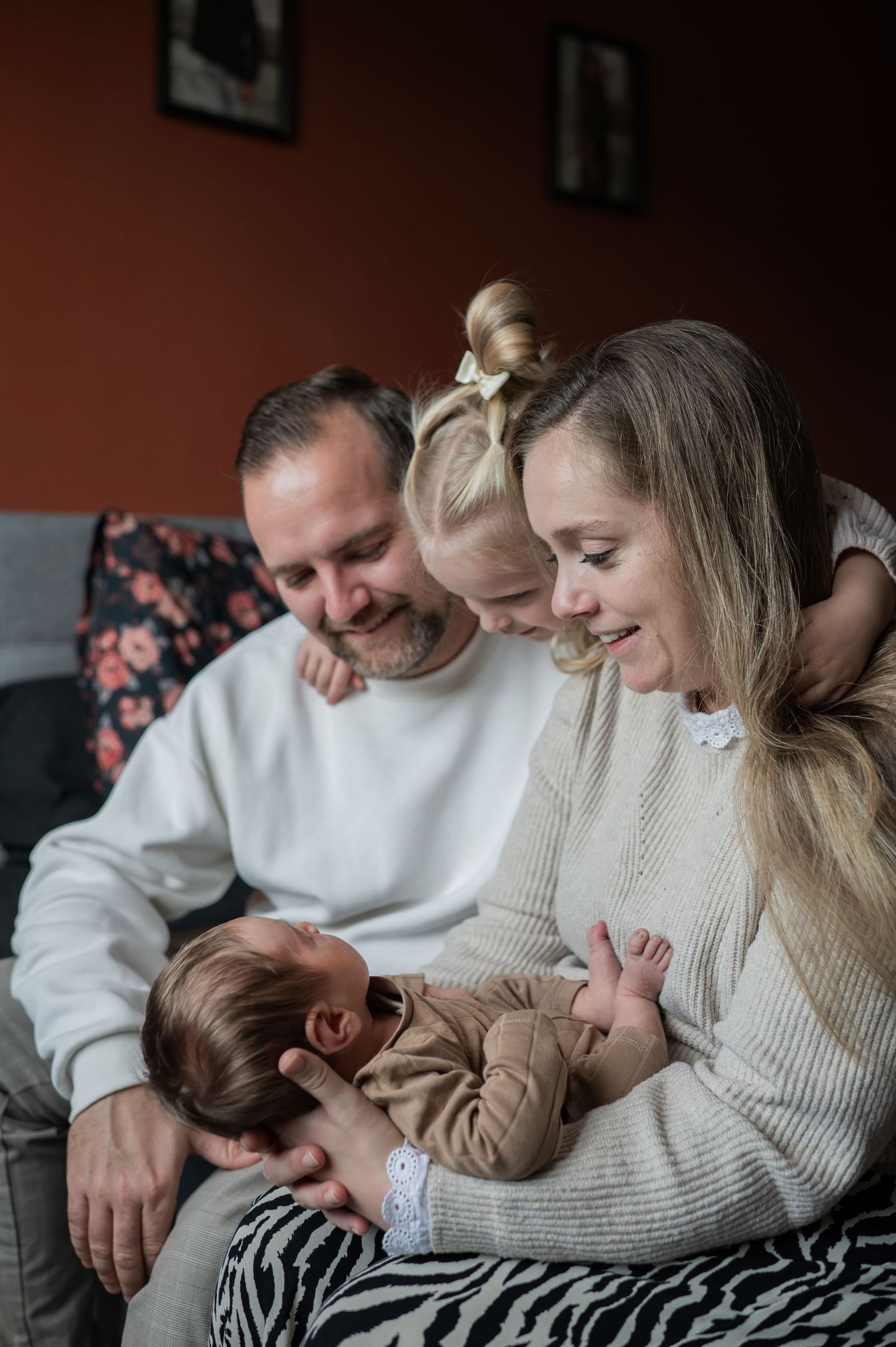 Happy family of four with a newborn baby and young daughter sitting together on a sofa. Lelystad, Almere, Dronten, Flevoland