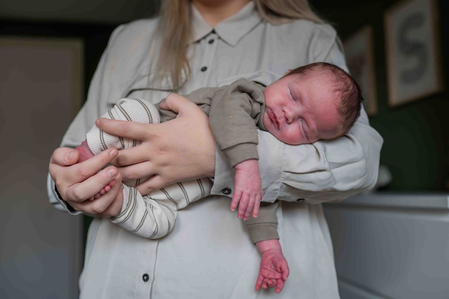 Mother cradling a sleeping newborn baby in her arms, showing the tiny infant up close.