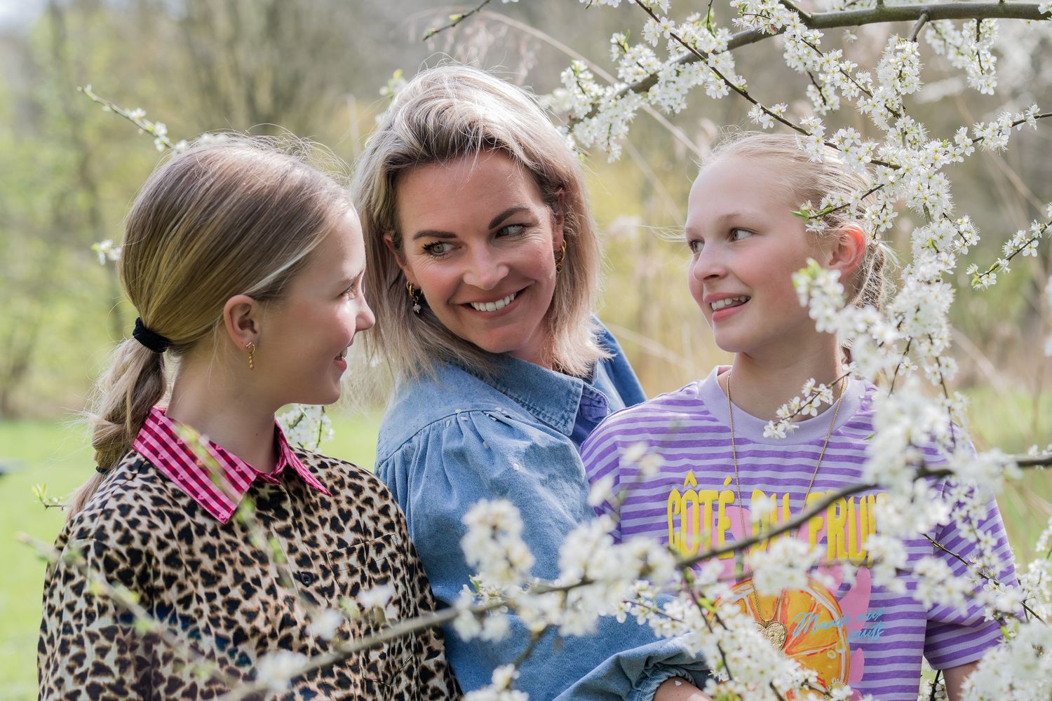 Woman and two girls admiring white spring blossoms on a flowering tree outdoors.