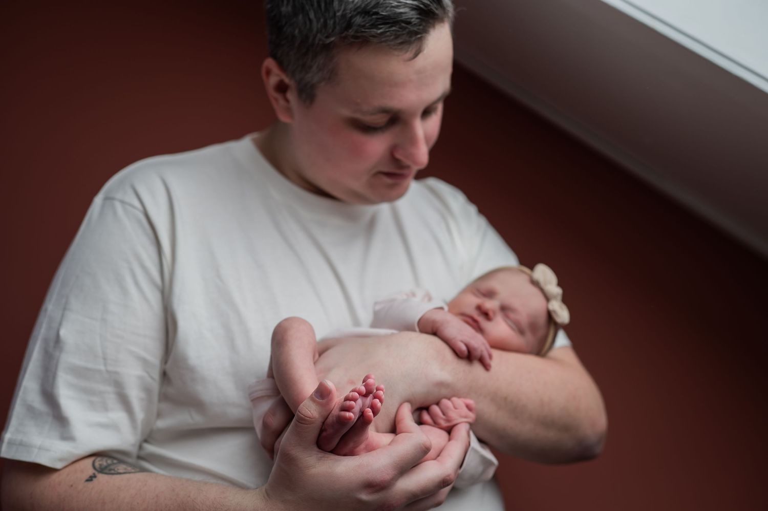 Father tenderly cradling his newborn baby in both hands, gazing lovingly at the infant in a hospital room.