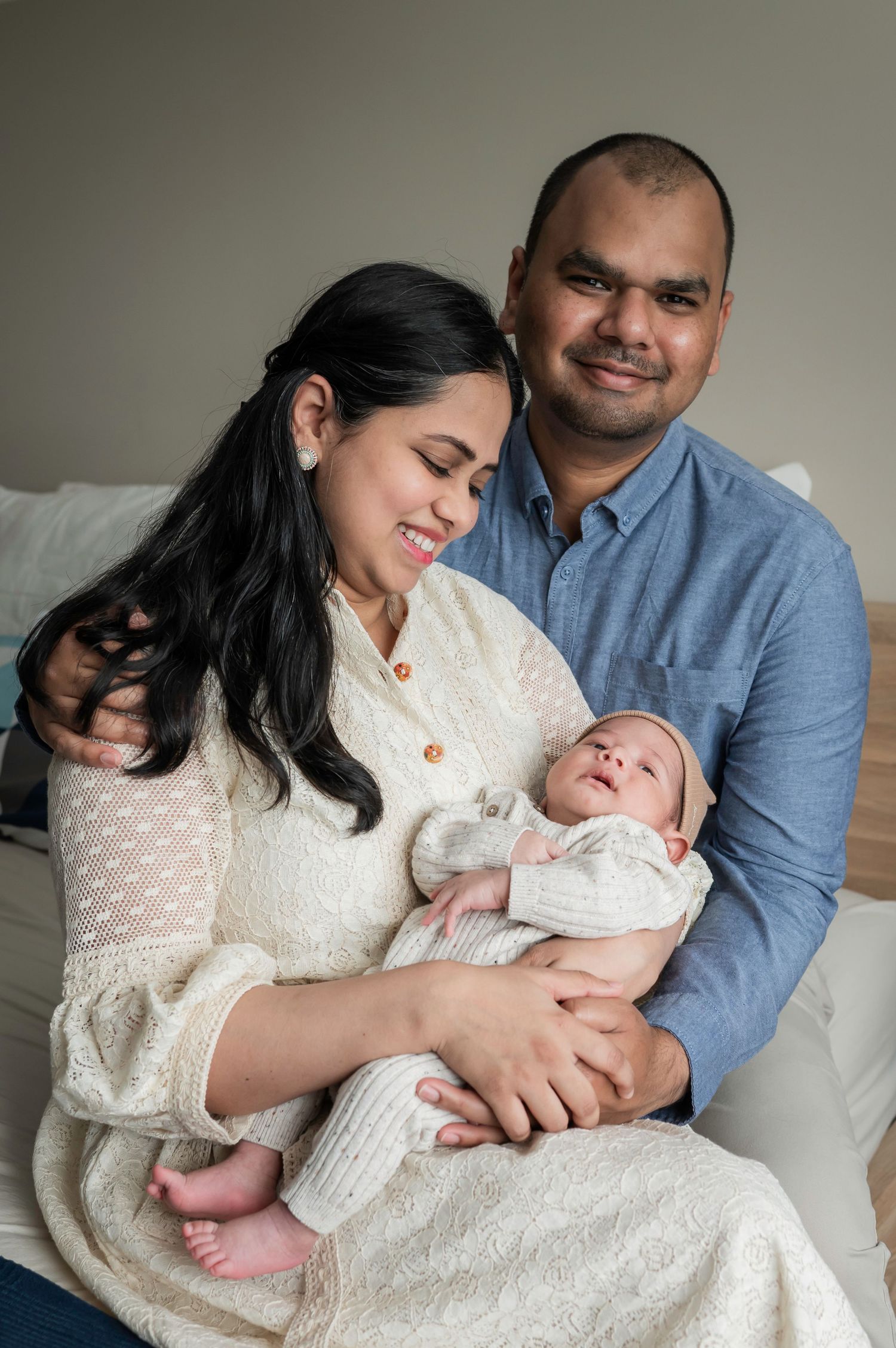 Happy couple sitting on bed smiling at their newborn baby wrapped in white, a tender family portrait. Lelystad, Almere, Dronten, Flevoland