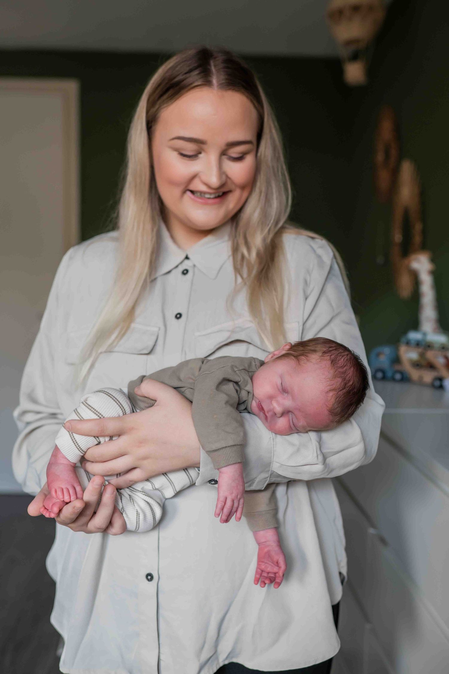 Smiling blonde mother holds her sleeping newborn baby in her arms at home. Lelystad, Almere, Dronten, Flevoland