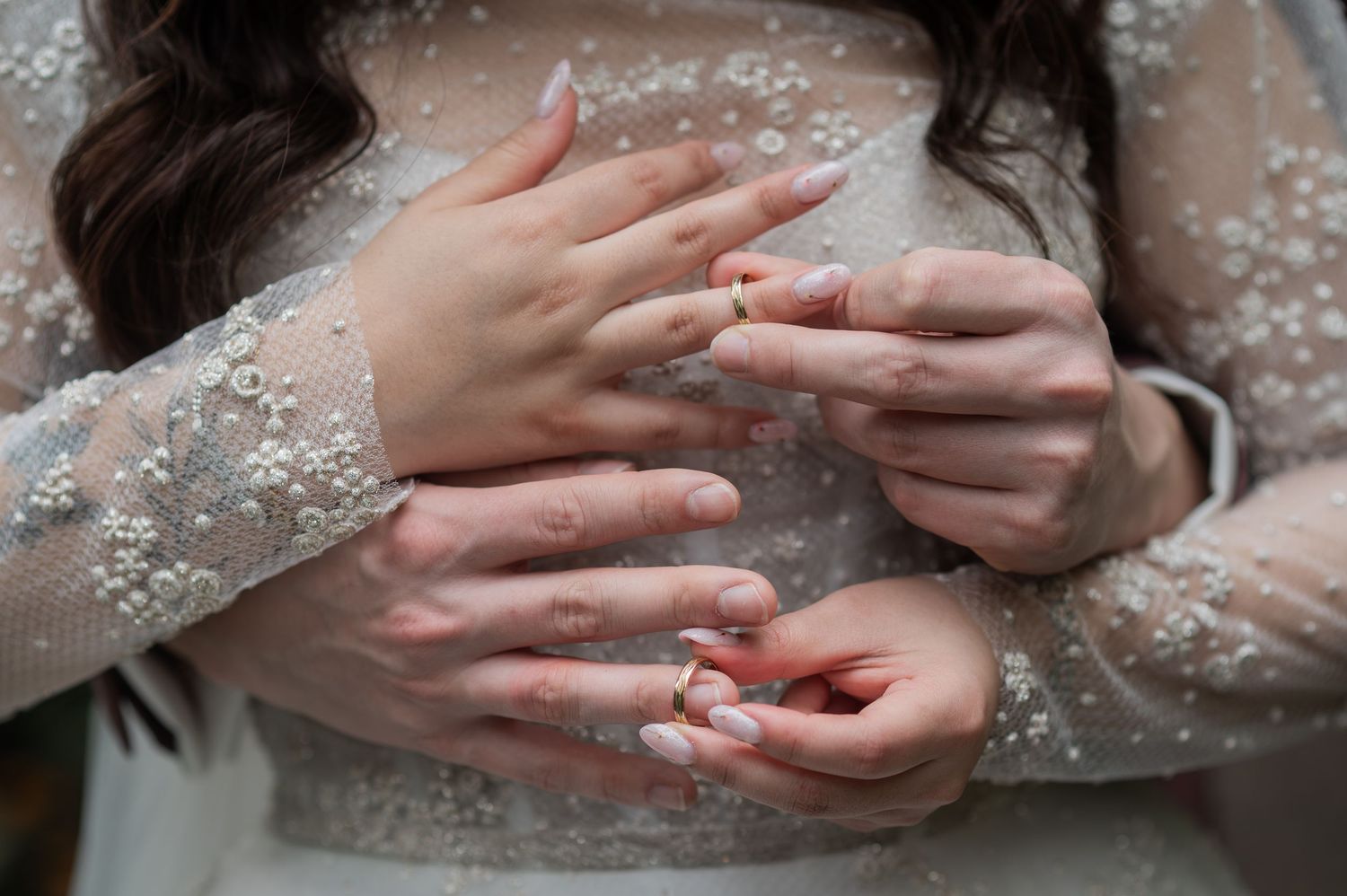 Bride in pearl-embellished lace gown holding wedding rings in her delicate hands with neutral manicure.
