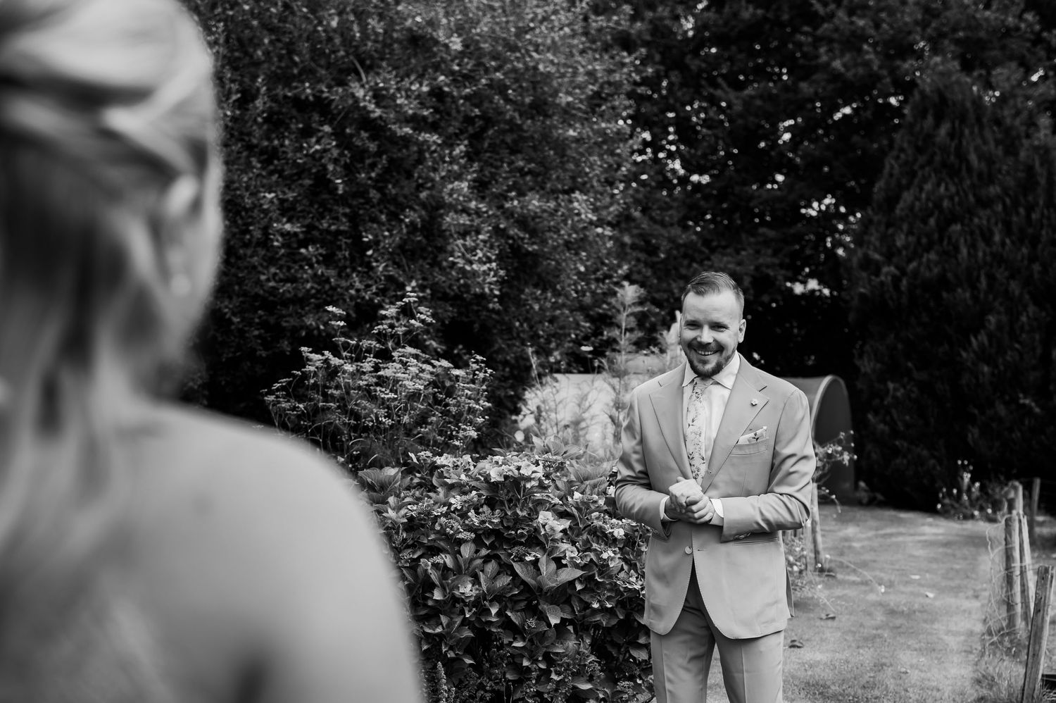 Groom smiling joyfully as bride approaches during an outdoor first look moment at a wedding.