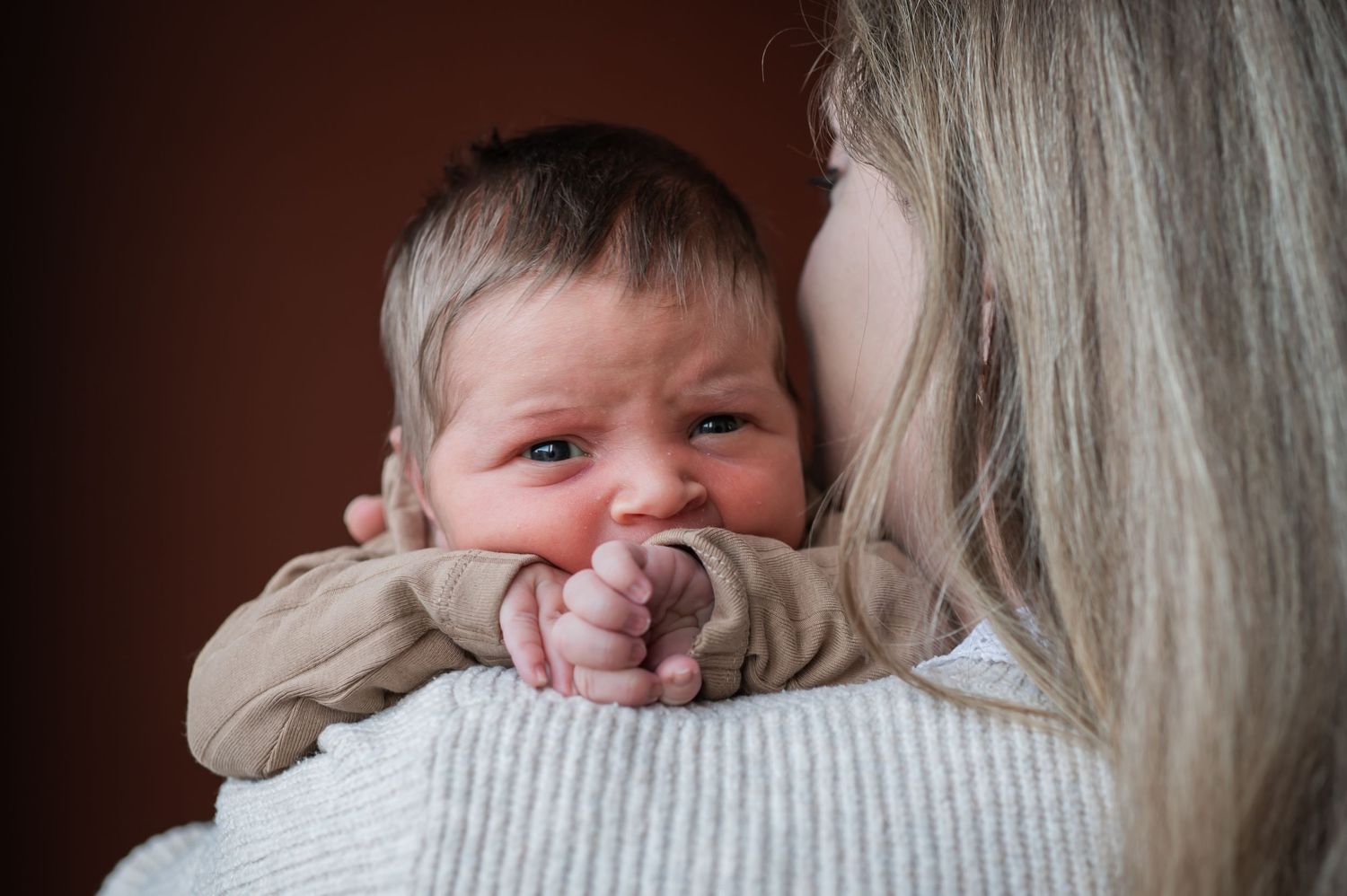 A mother tenderly holds her crying newborn baby against her shoulder, comforting the infant.