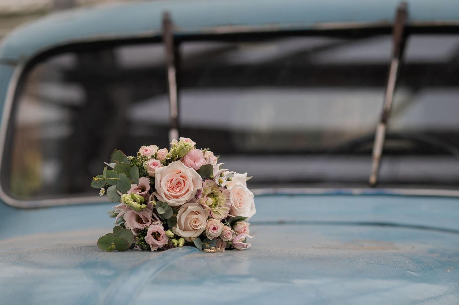 A delicate pink rose bouquet resting on a vintage light blue car hood at a wedding.