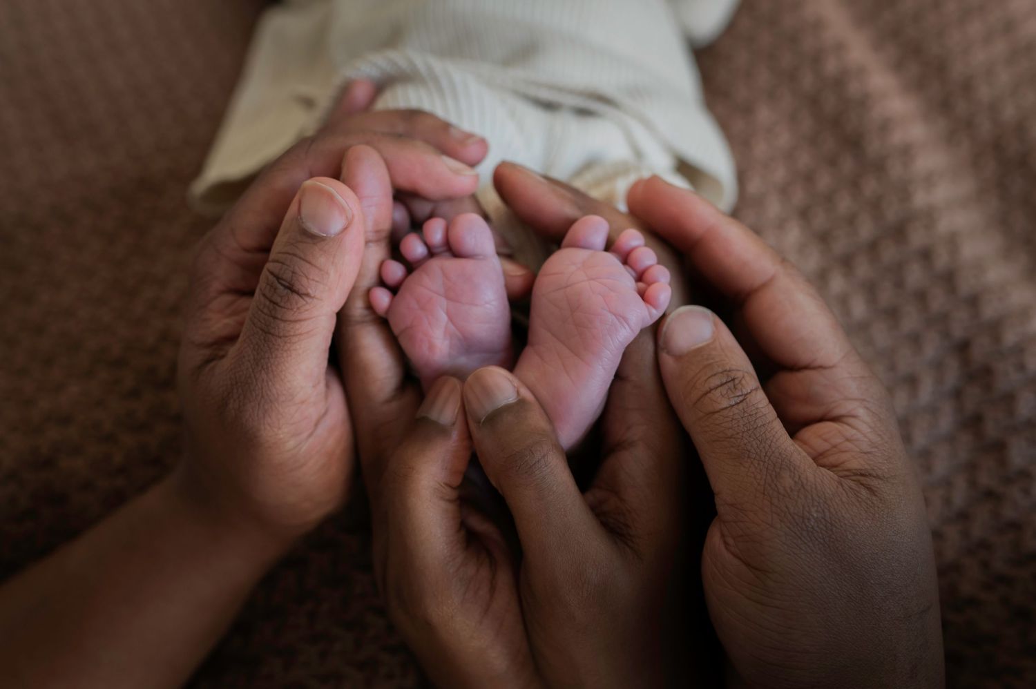 Parents gently cradling their newborn baby's tiny feet in their hands in a close-up photo. Lelystad, Almere, Dronten, Flevoland