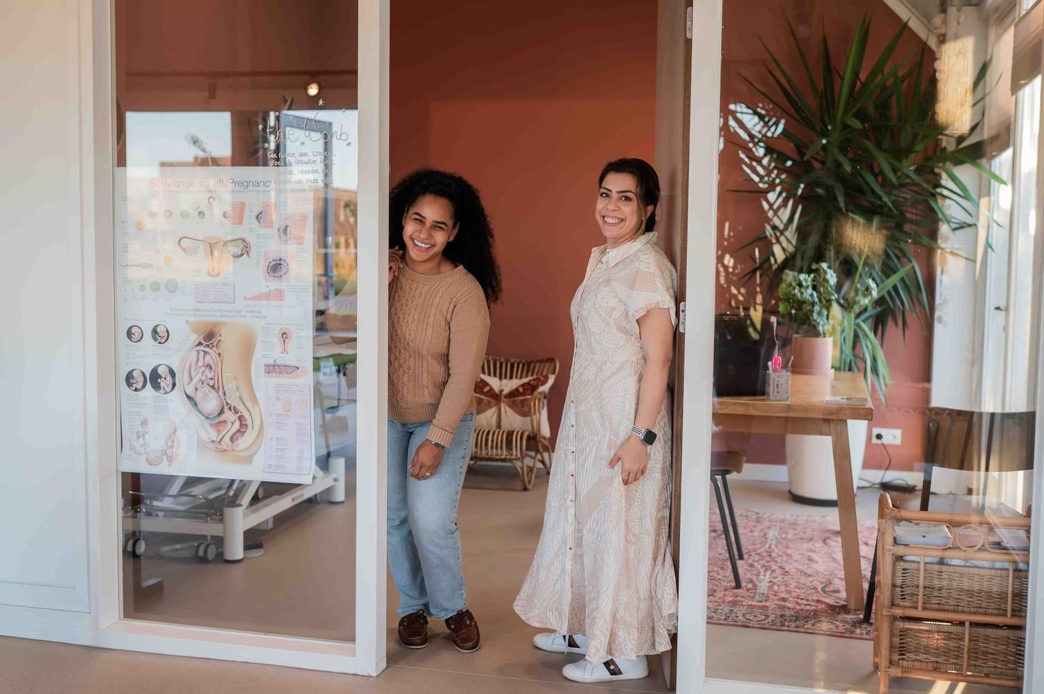 Two women smiling at the entrance of a modern boutique shop with pink interior decor.
