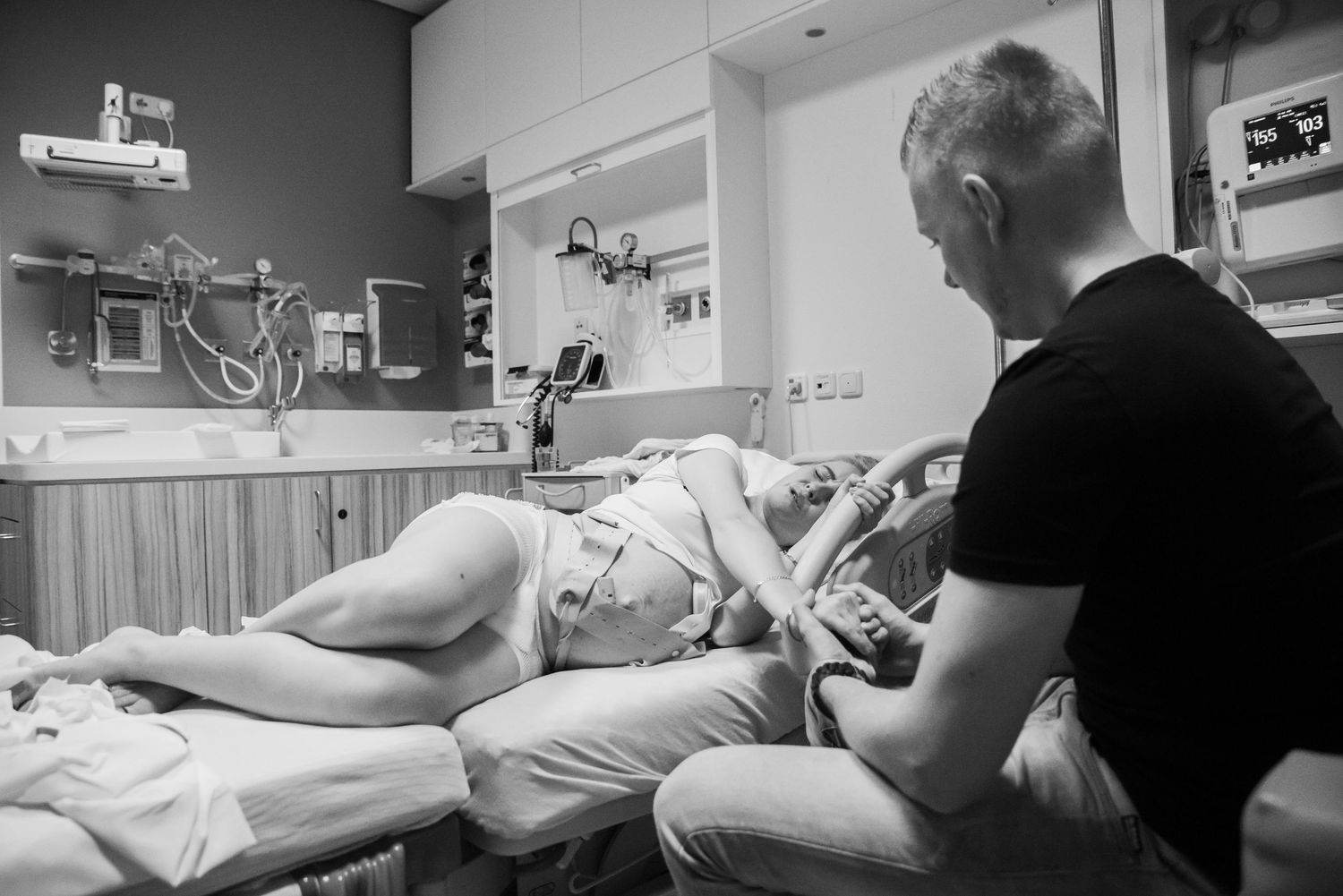 Black and white photo of a woman in labor lying on a hospital bed with a supportive partner beside her.